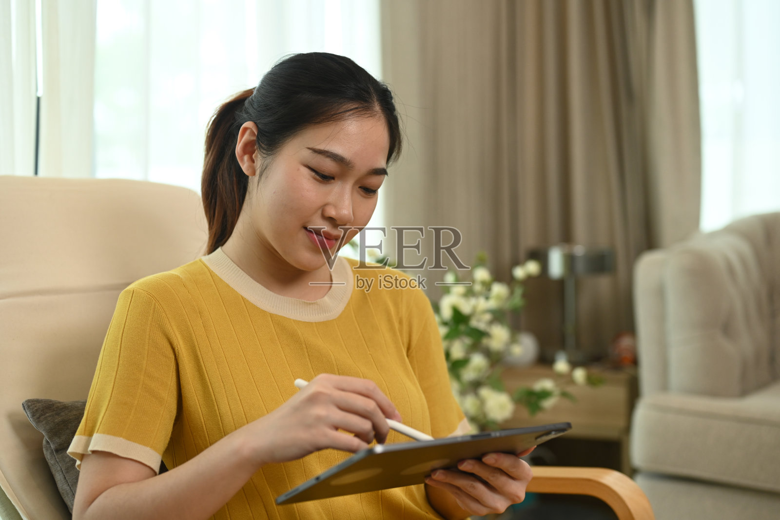 亚洲女性自由职业者的肖像,坐在客厅的椅子上用数码平板电脑工作照片摄影图片