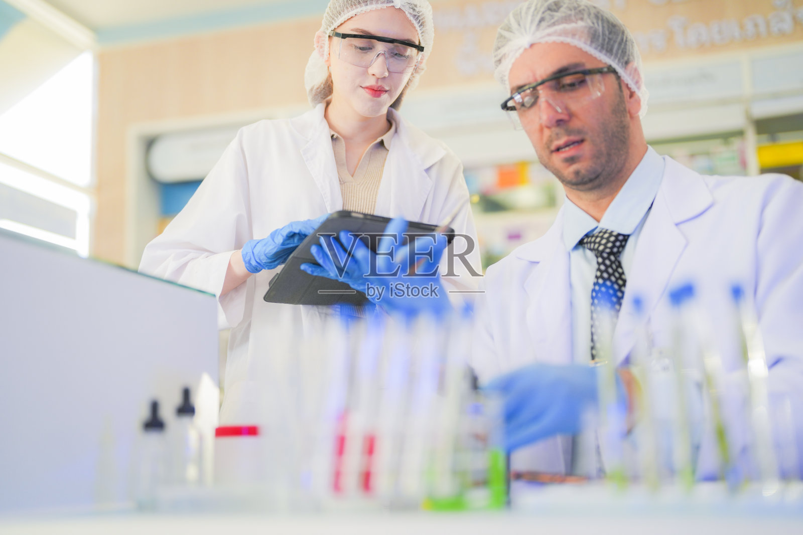 科学家进行实验并记录数据。人们为生产药物和生物化学而安排试管和化学品设备。人们拿着装有化学液体和植物样品的管子。照片摄影图片