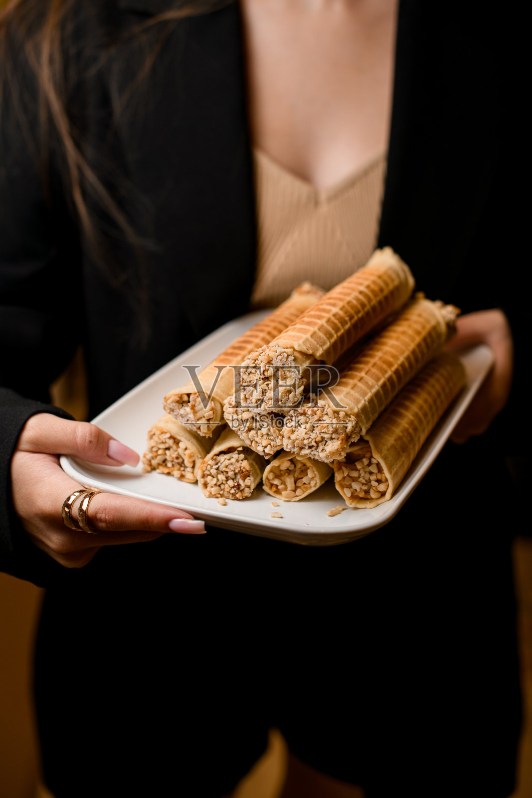 一个穿着黑色衣服,留着棕色长发的女孩手里拿着盛着薄饼卷的白色盘子照片摄影图片