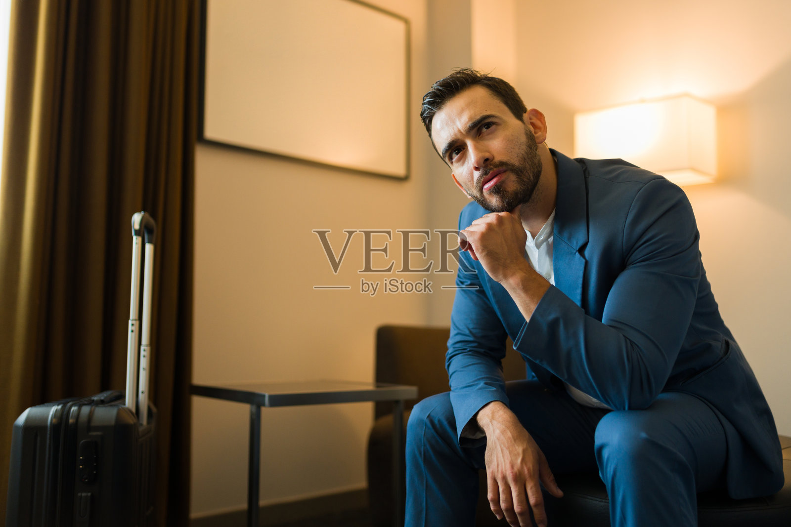 迷人的商人坐在酒店房间的行李箱旁,陷入了沉思照片摄影图片