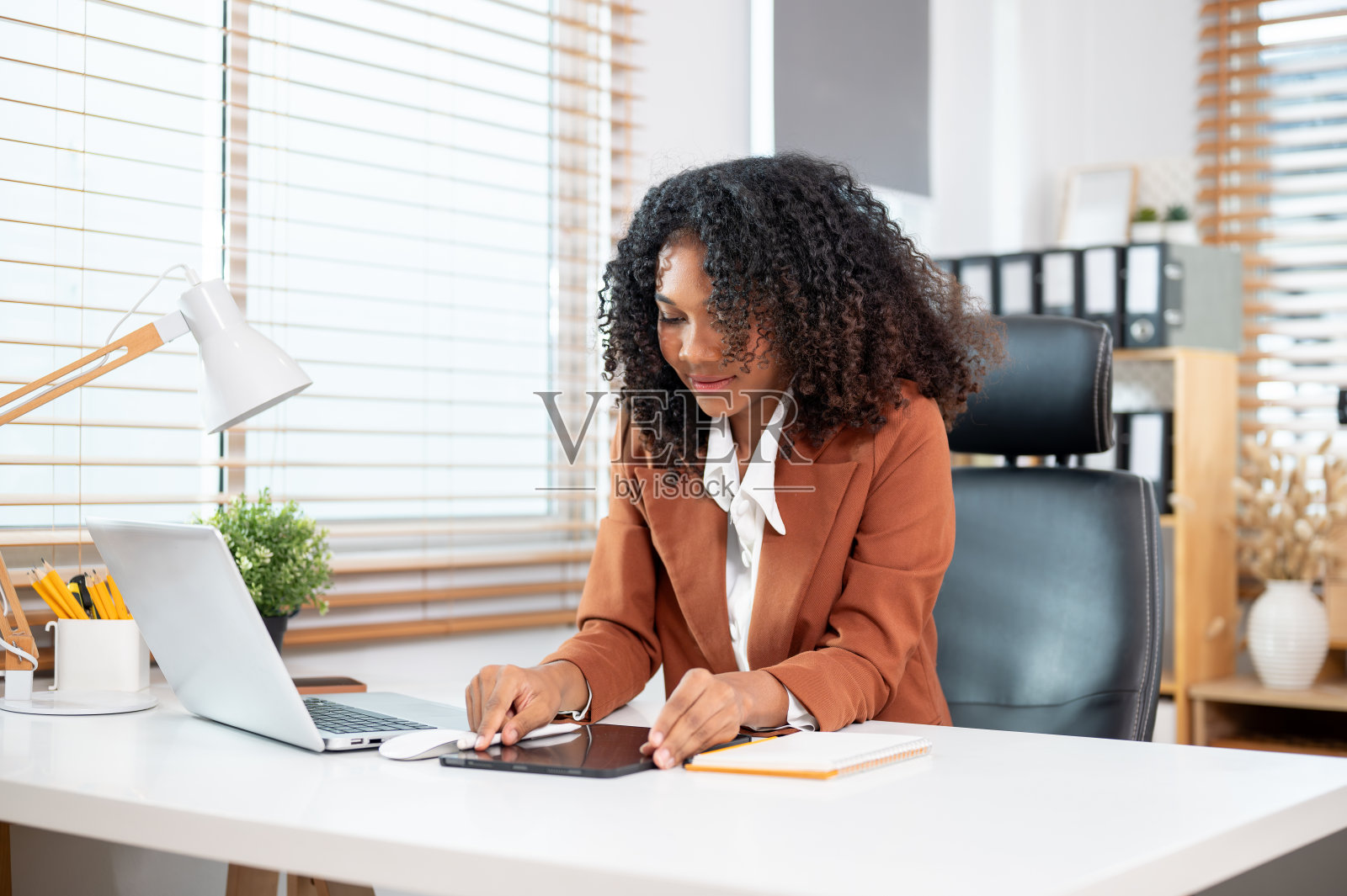 一位有魅力、积极向上的黑人女商人正在办公室的办公桌前使用她的电子平板电脑。照片摄影图片