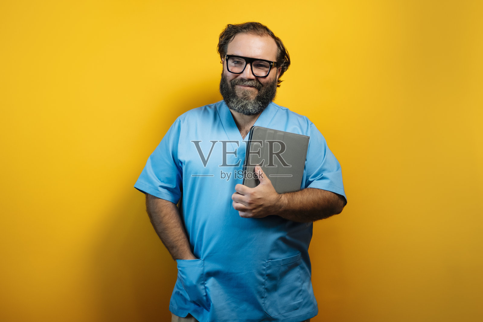 医生穿着黄色背景的蓝色外套,腋下夹着一块药片。医院使用技术的概念。照片摄影图片