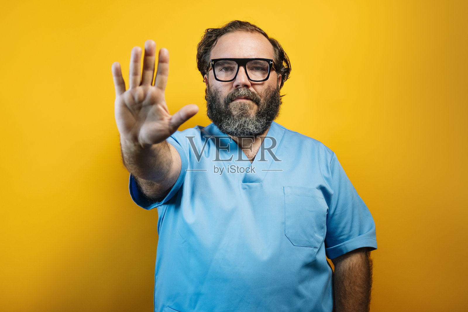 在黄色背景上穿蓝色外套的医生做了一个停止的手势。照片摄影图片