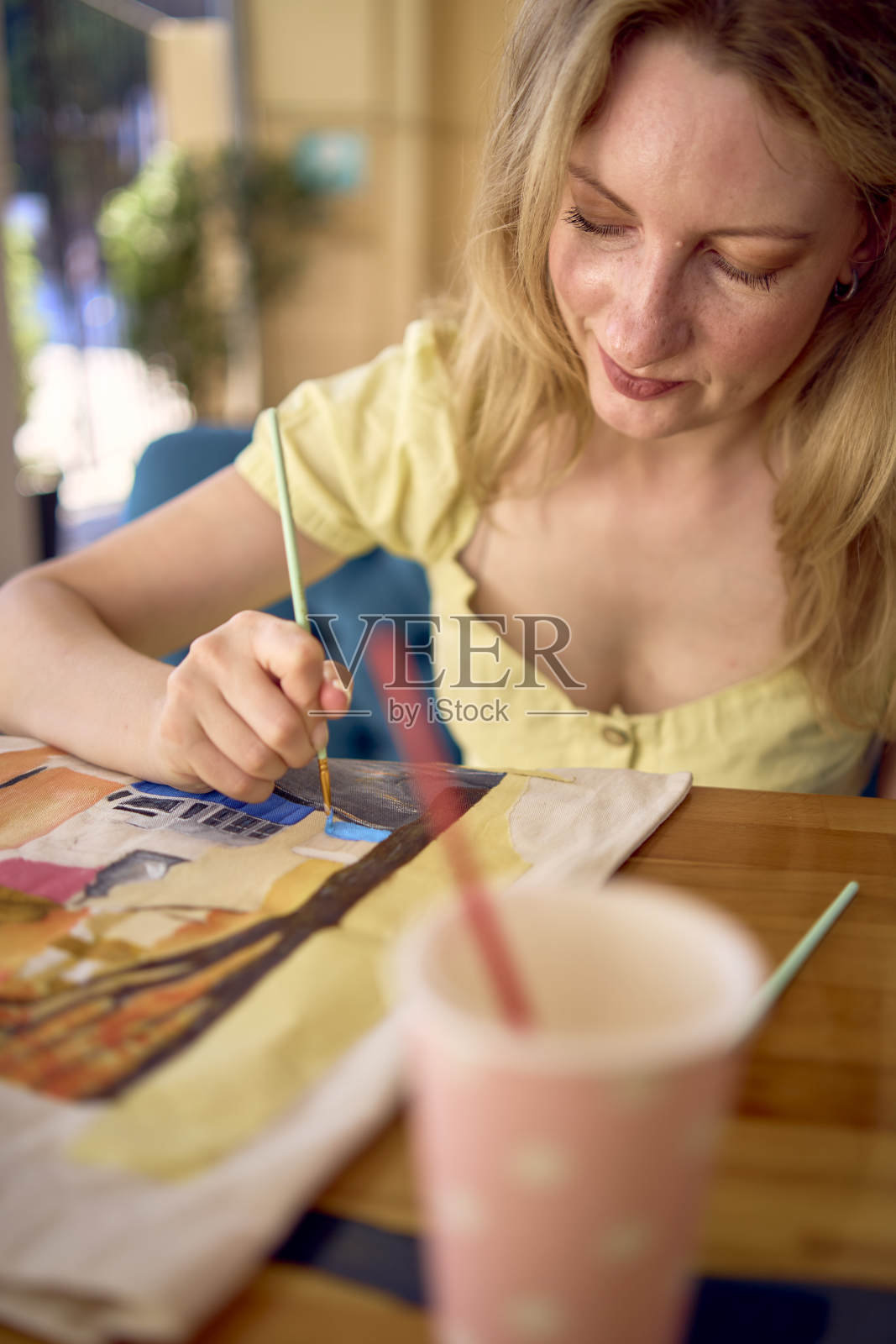 一位穿着黄色连衣裙的年轻漂亮的艺术家正在画一个定制的购物袋照片摄影图片