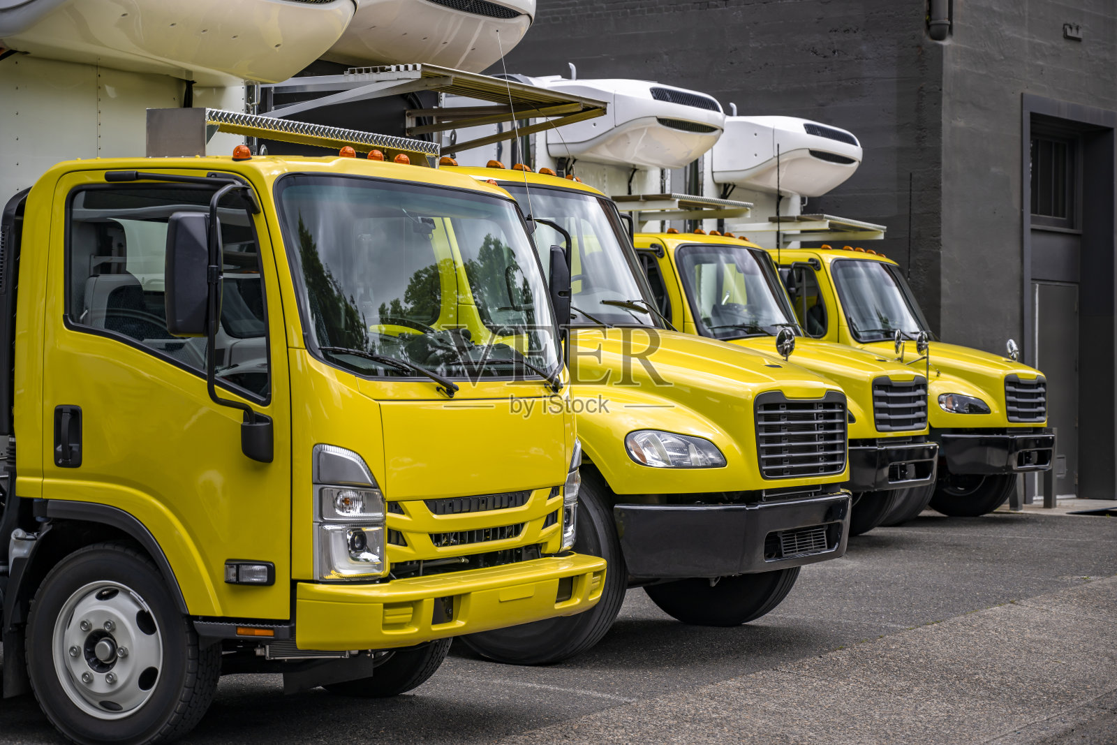 在工业仓库的停车场上,排着一排用于本地交货的中型半挂车和冷藏箱拖车照片摄影图片