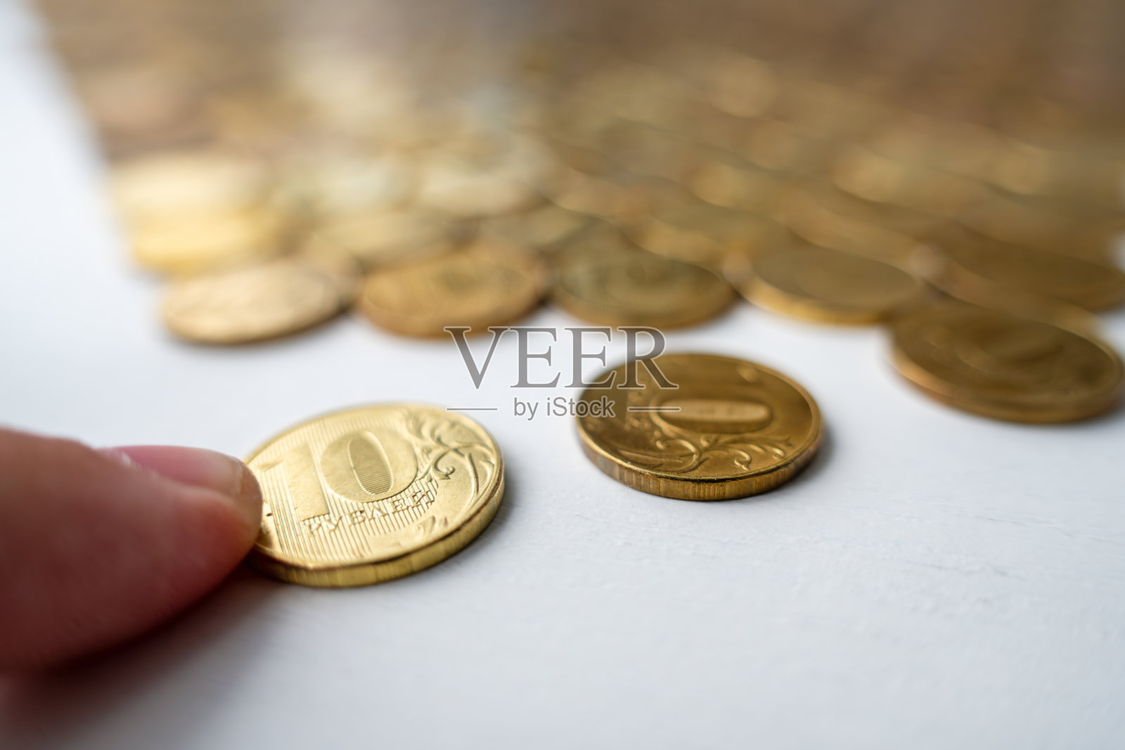 男人的手拿着一枚硬币。浪费积蓄。手把卢布硬币放在白底的钱堆上照片摄影图片