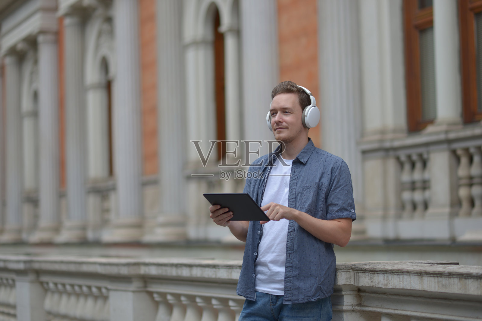 维也纳街头,一名年轻男子手持平板电脑,戴着耳机听音乐。放松享受的生活理念照片摄影图片