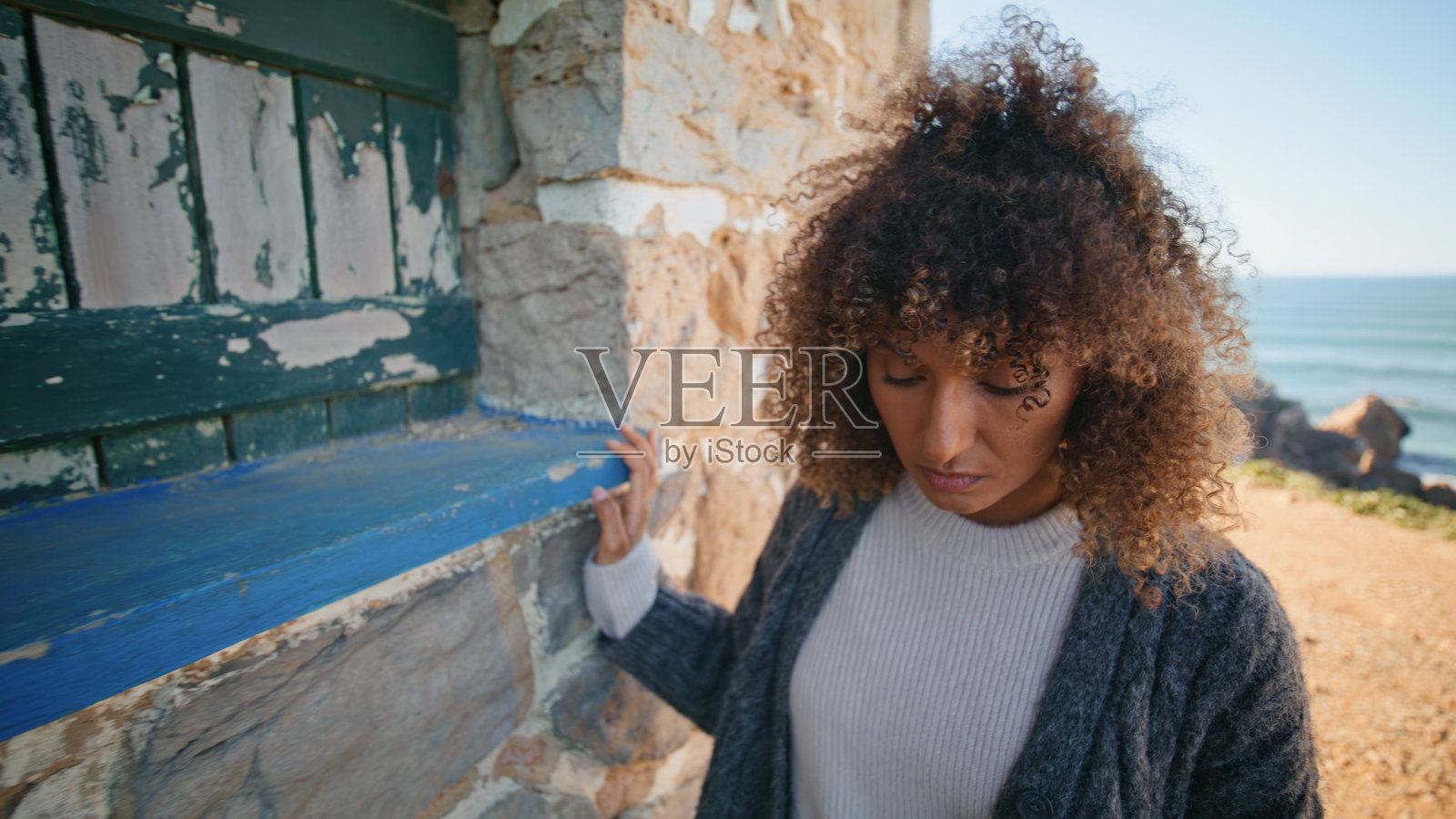 沉思着石砌建筑特写镜头的沮丧女士,卷发黑发模特摆姿势照片摄影图片