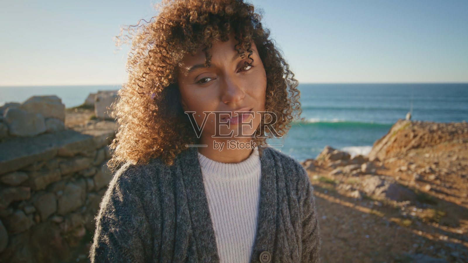 温柔的黑发女郎摆海崖享受自然的肖像。卷发女人放松照片摄影图片