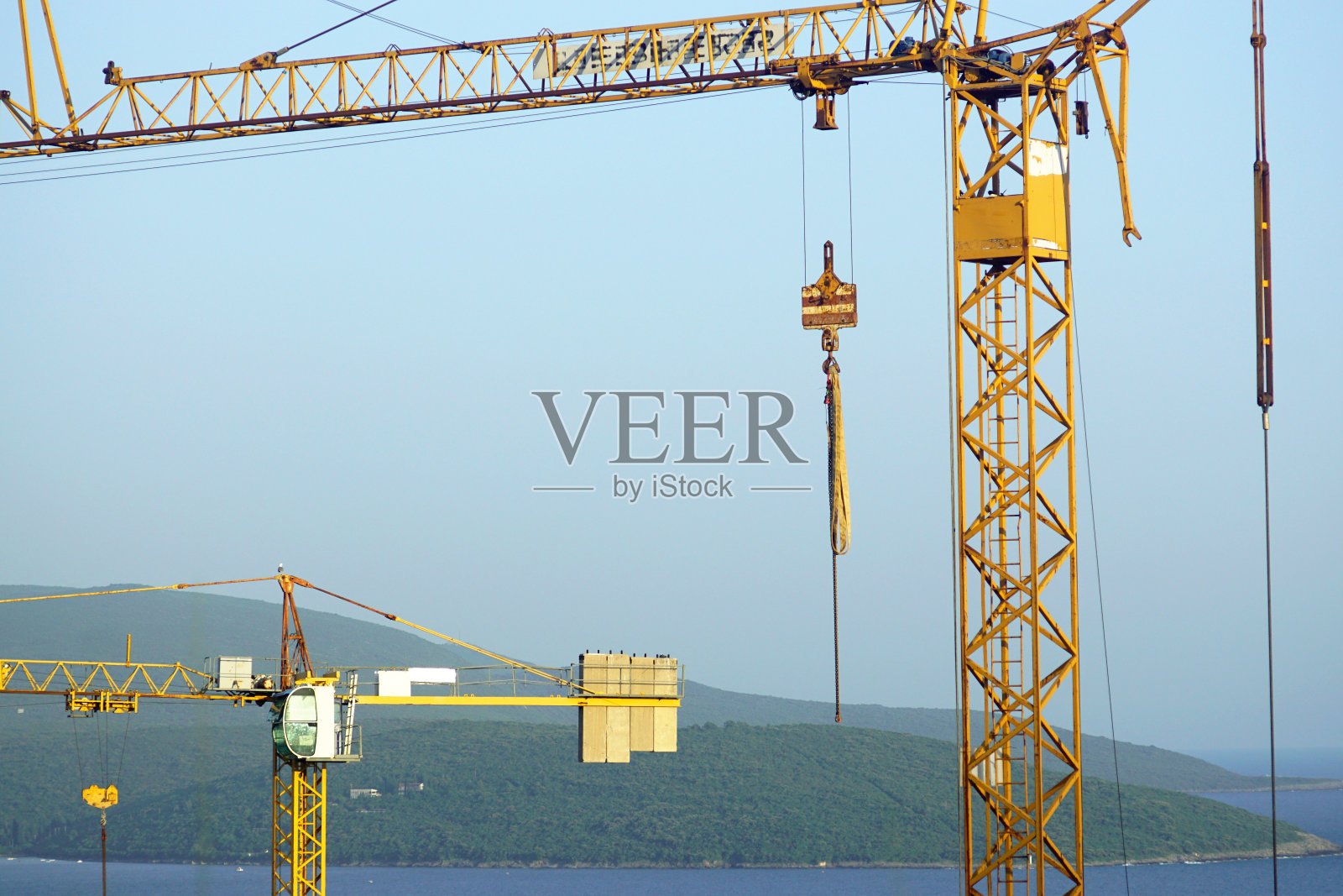 两个塔式起重机的上部在大海和山脉的背景下-在海岸上建造房屋。照片摄影图片