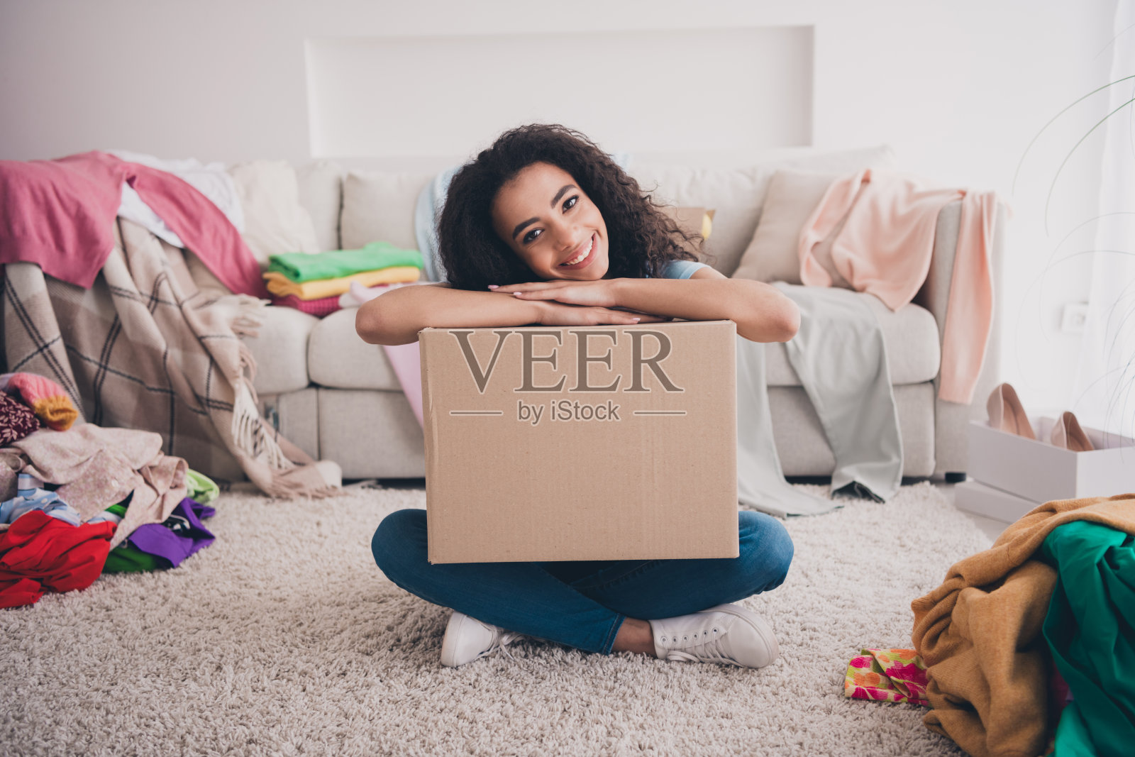 漂亮的年轻女孩的全尺寸照片坐在地毯地板微笑拿衣服东西盒子公寓室内照片摄影图片