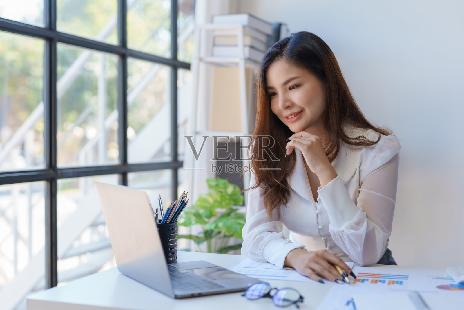 专业的亚洲商人,带着自信的微笑,在明亮的办公室里,带着笔记本电脑和文件。照片摄影图片