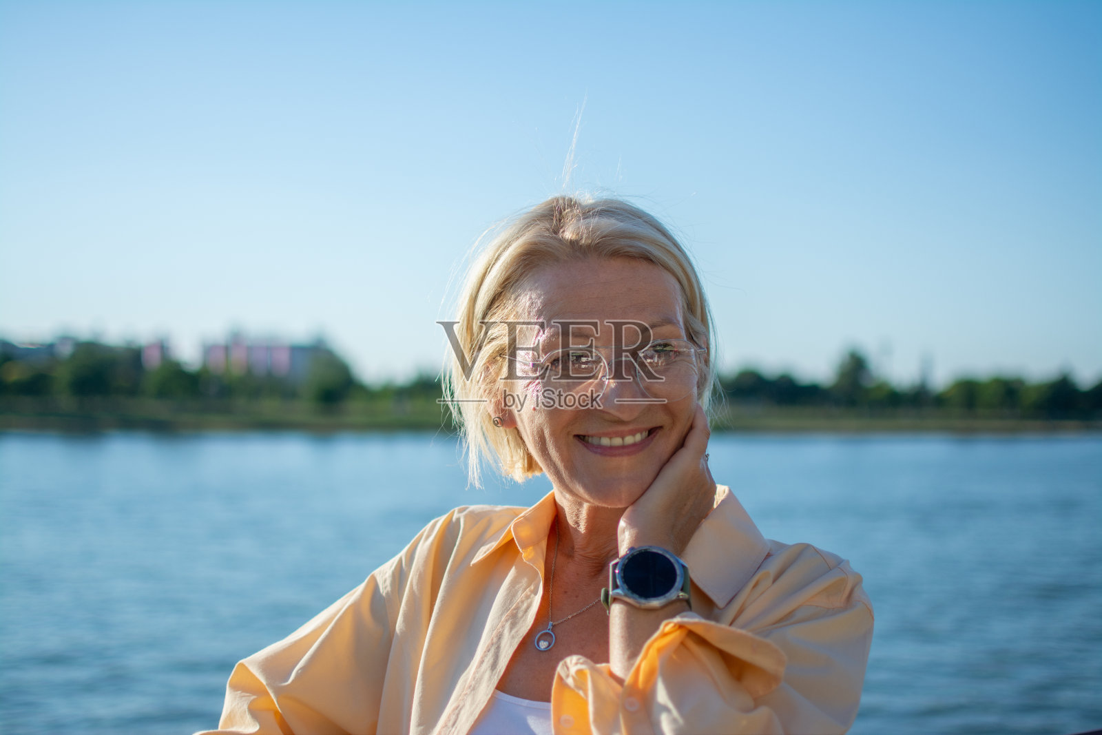 面带微笑的成熟金发女人的肖像,戴着眼镜站在河边照片摄影图片