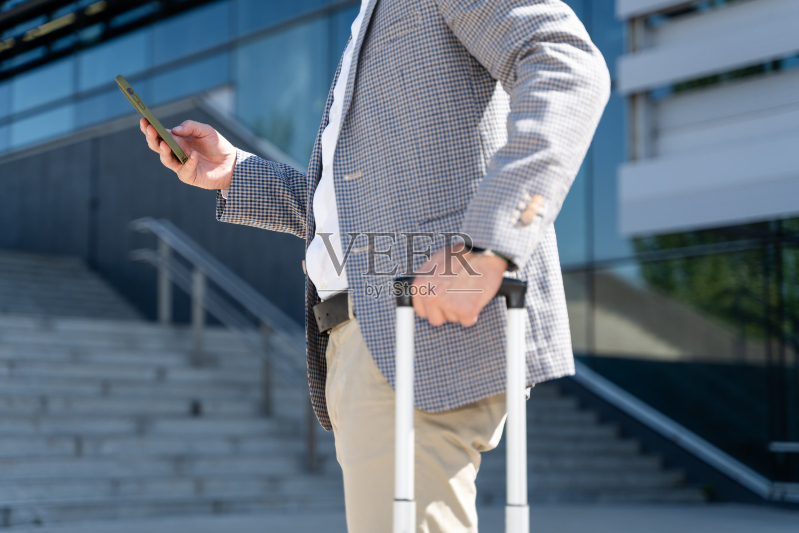 在办公楼外用智能手机提着行李箱的商人照片摄影图片