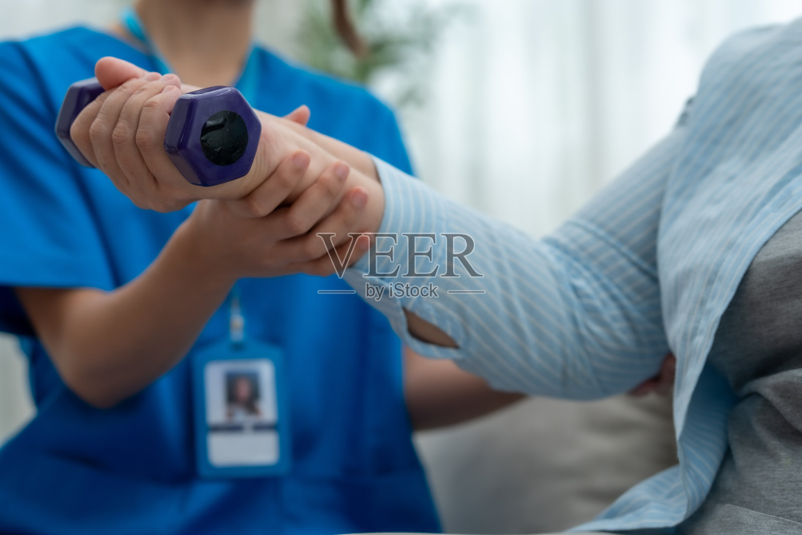 一位穿着蓝色制服的专业护理人员帮助一位老年患者在家中使用哑铃进行物理治疗练习。照片摄影图片