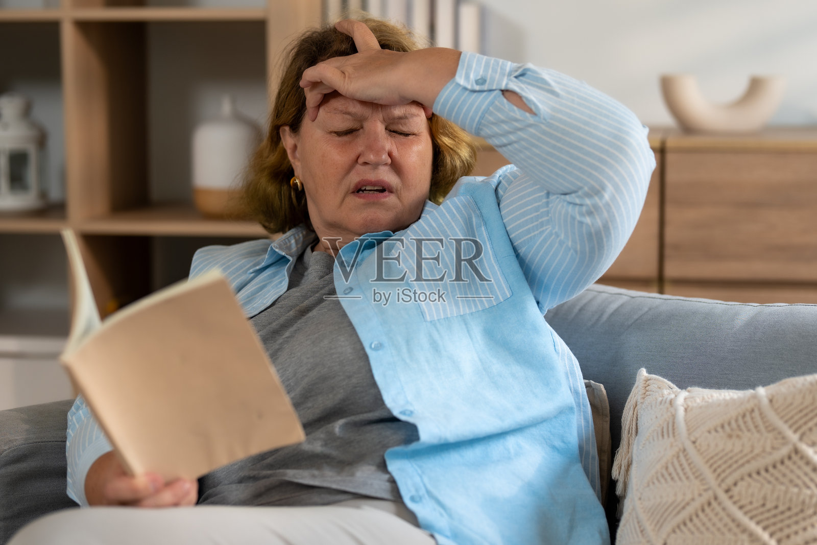 在舒适的客厅里,一位老妇人抱着额头看书,感觉不舒服。照片摄影图片