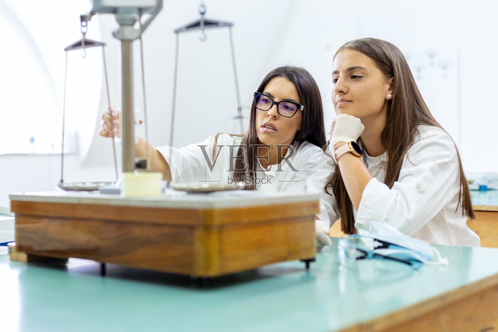 两个女人在实验室里摆弄老式天平。照片摄影图片