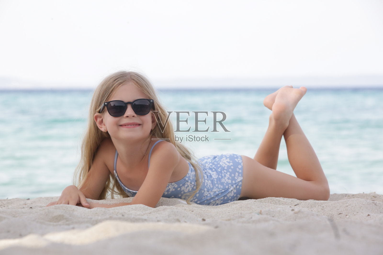 可爱的小女孩穿着蓝色泳装和黑色太阳镜在沙滩上照片摄影图片