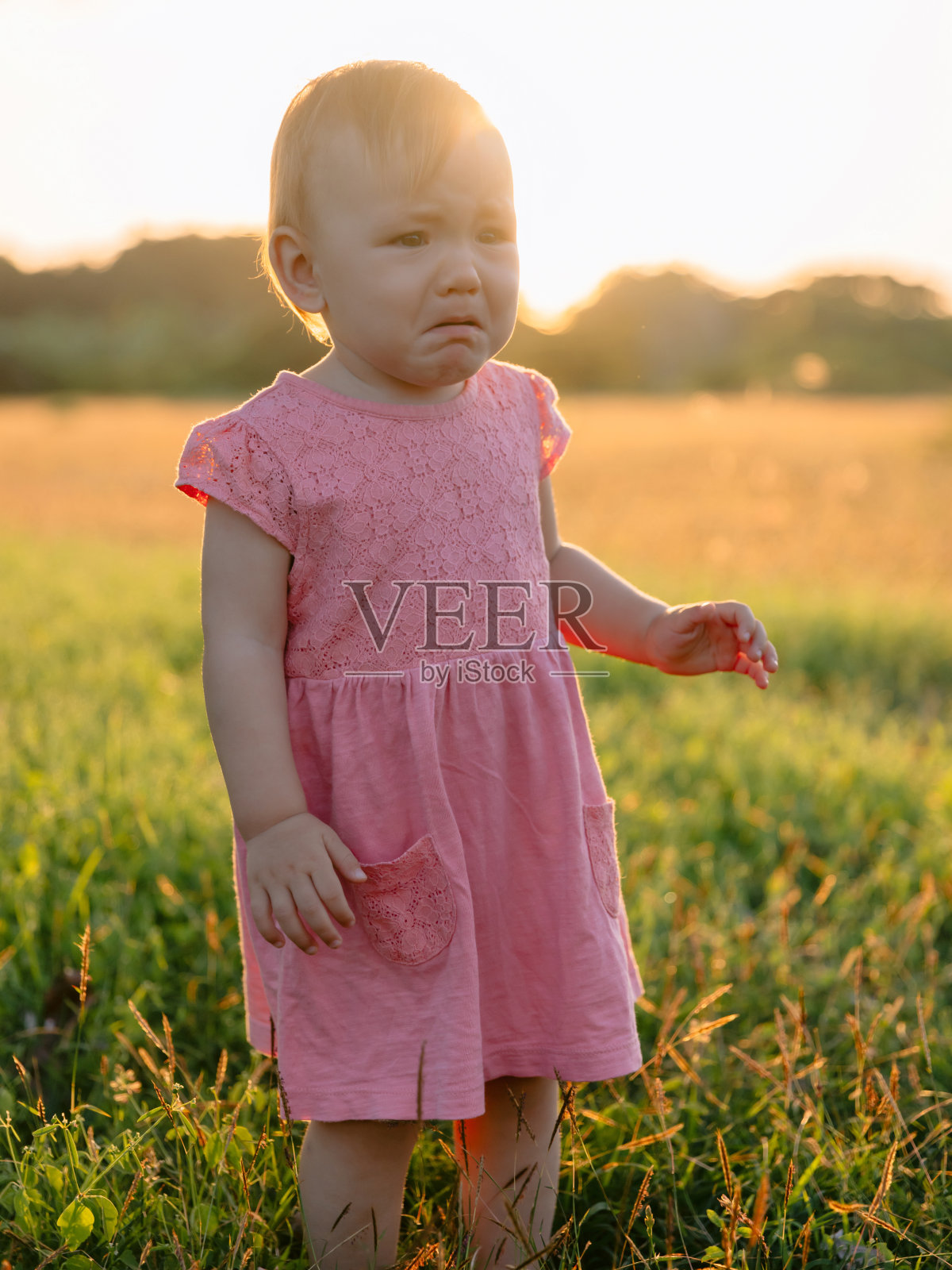 在公园里穿着粉红色裙子哭泣的婴儿。在夕阳色调的户外,婴儿女孩。照片摄影图片