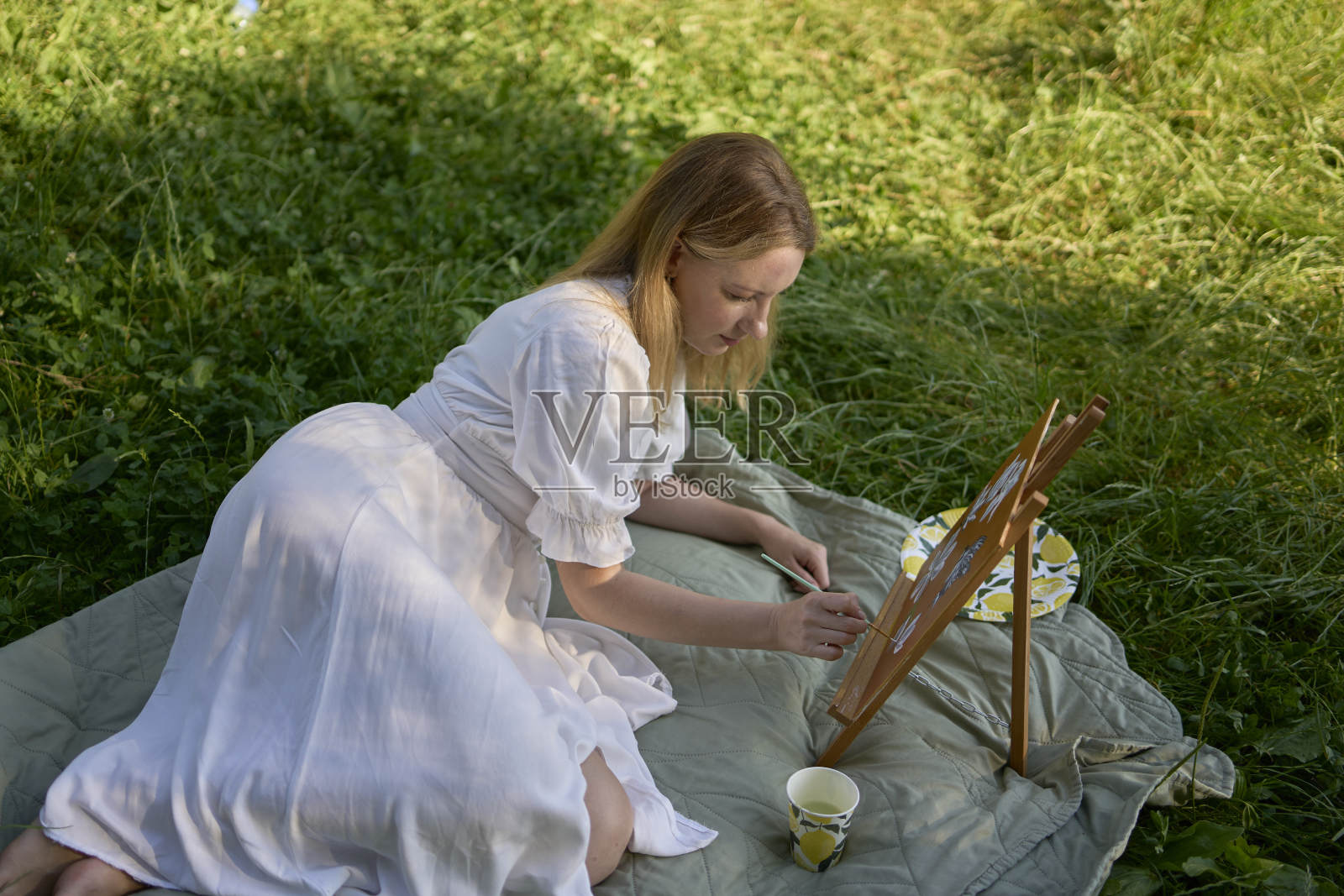 一位穿着白色连衣裙的年轻漂亮的画家在河岸上画画照片摄影图片