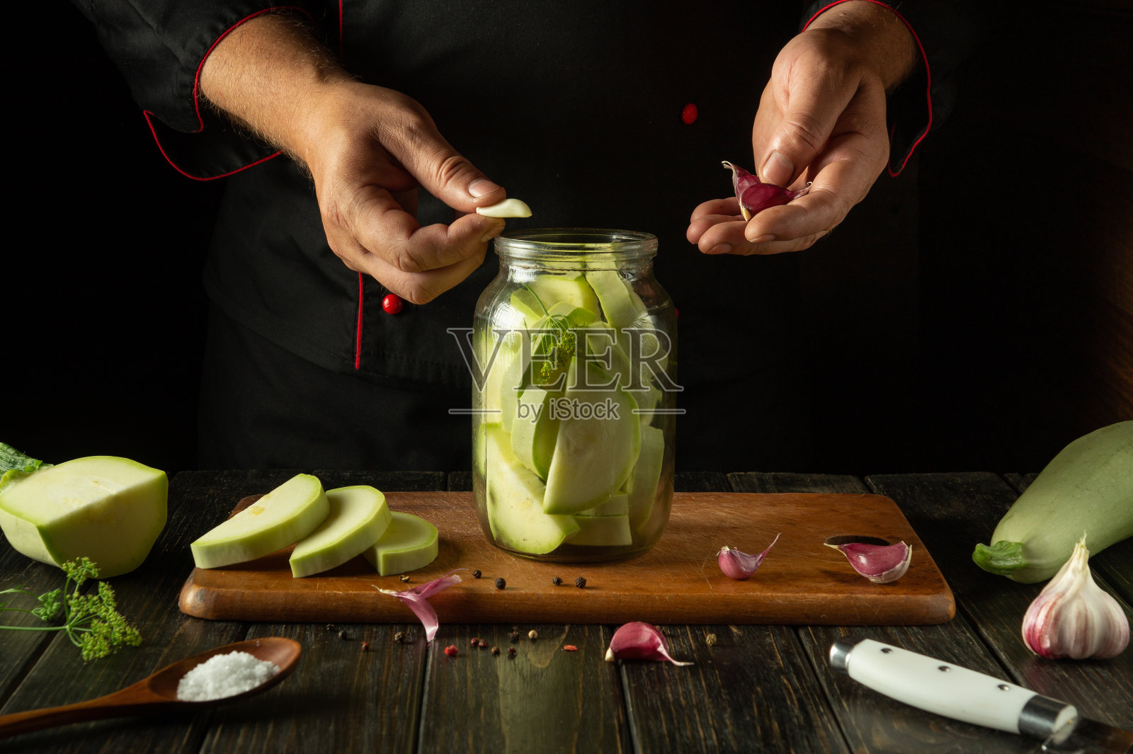 用香料和大蒜腌制西葫芦。厨师将一瓣大蒜放入一个装有腌蔬菜骨髓的罐子里照片摄影图片