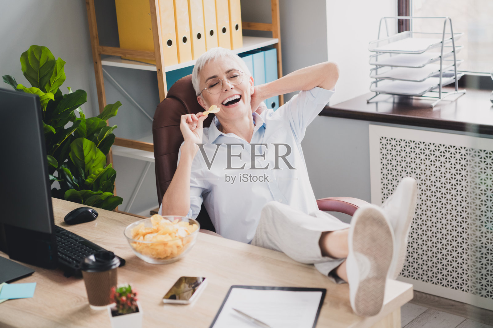 迷人的好心情的照片年龄招聘女士穿着正式的衬衫在室内享受薯片工作工作站照片摄影图片