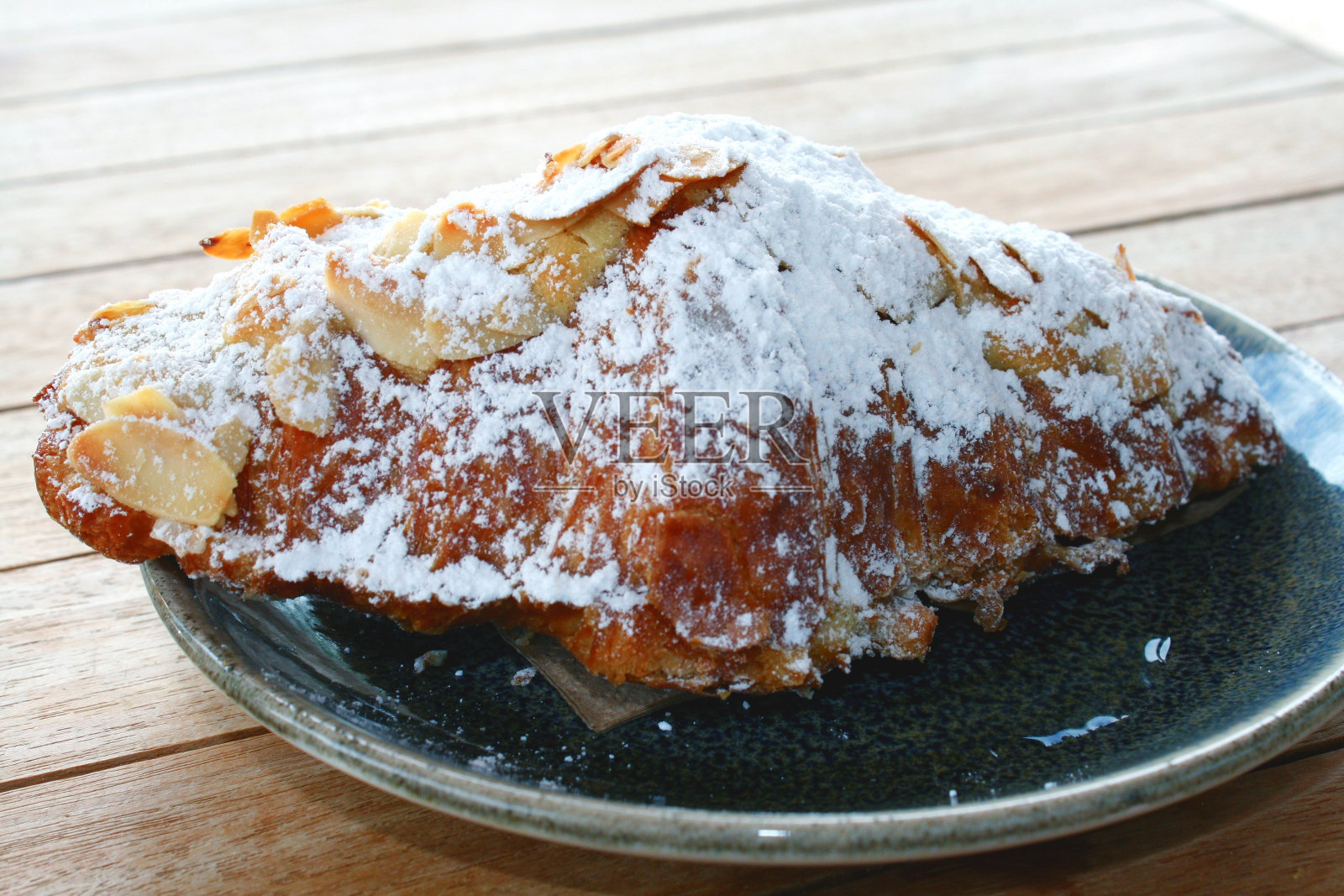 杏仁牛角包和糖粉放在深绿色盘子里。特写与选定的焦点。照片摄影图片