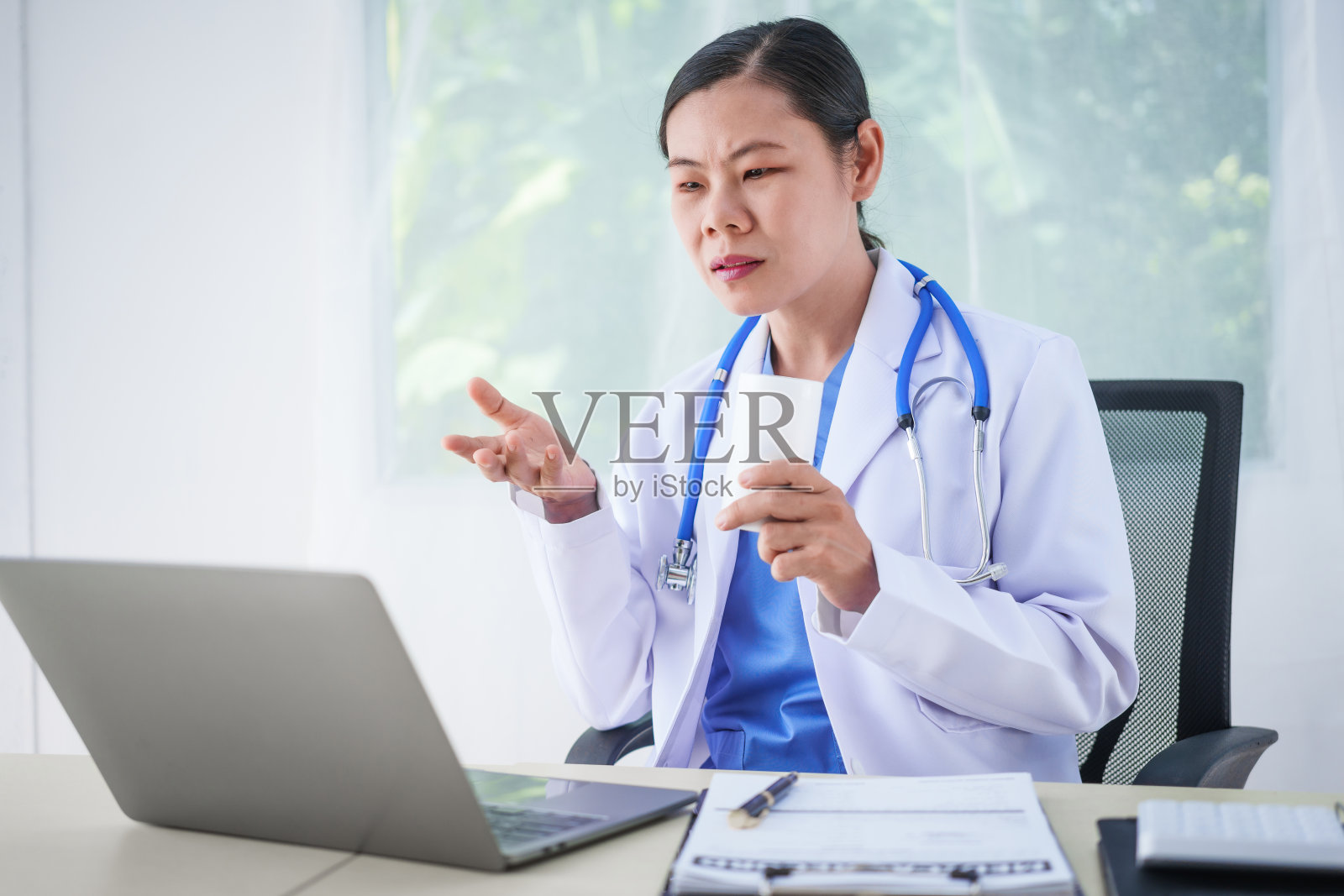 一位亚洲女医生坐在她的办公桌前,正在进行在线咨询。这种更快、更便宜、更方便的方法有助于预防疾病传播,并提供更容易获得医疗保健的途径。照片摄影图片