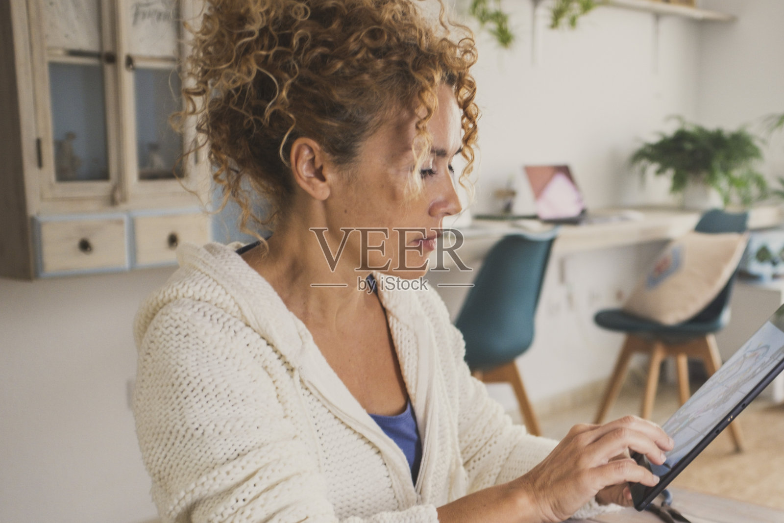 一名年轻成熟的妇女在家里为网上商业活动制作珠宝和项链。女人们坐在公寓的桌子旁做串珠爱好,独自拿着平板电脑进行室内休闲活动照片摄影图片