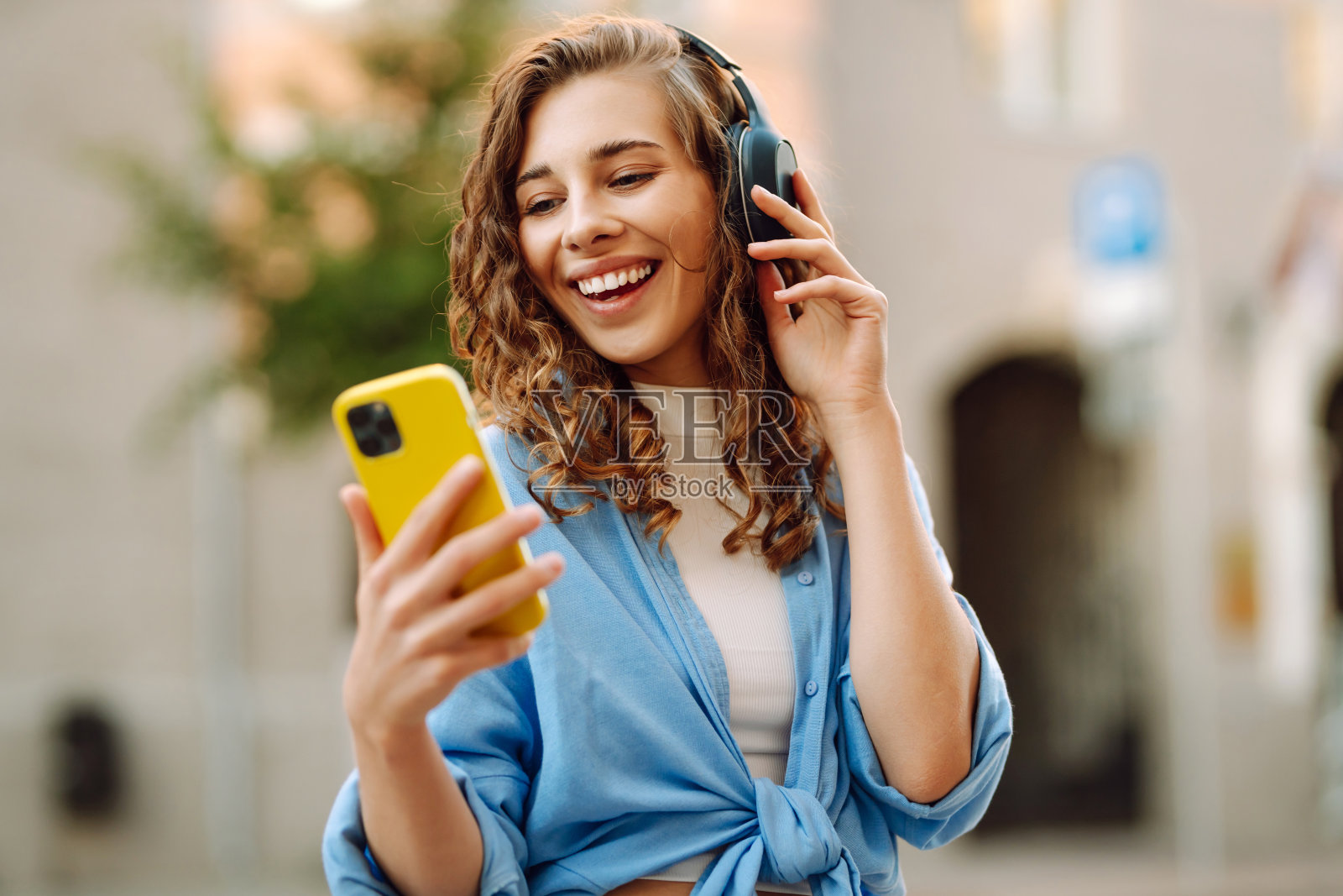 快乐轻松的女人在城市阳光明媚的街道上戴着无线耳机选择,聆听自己喜欢的音乐。照片摄影图片