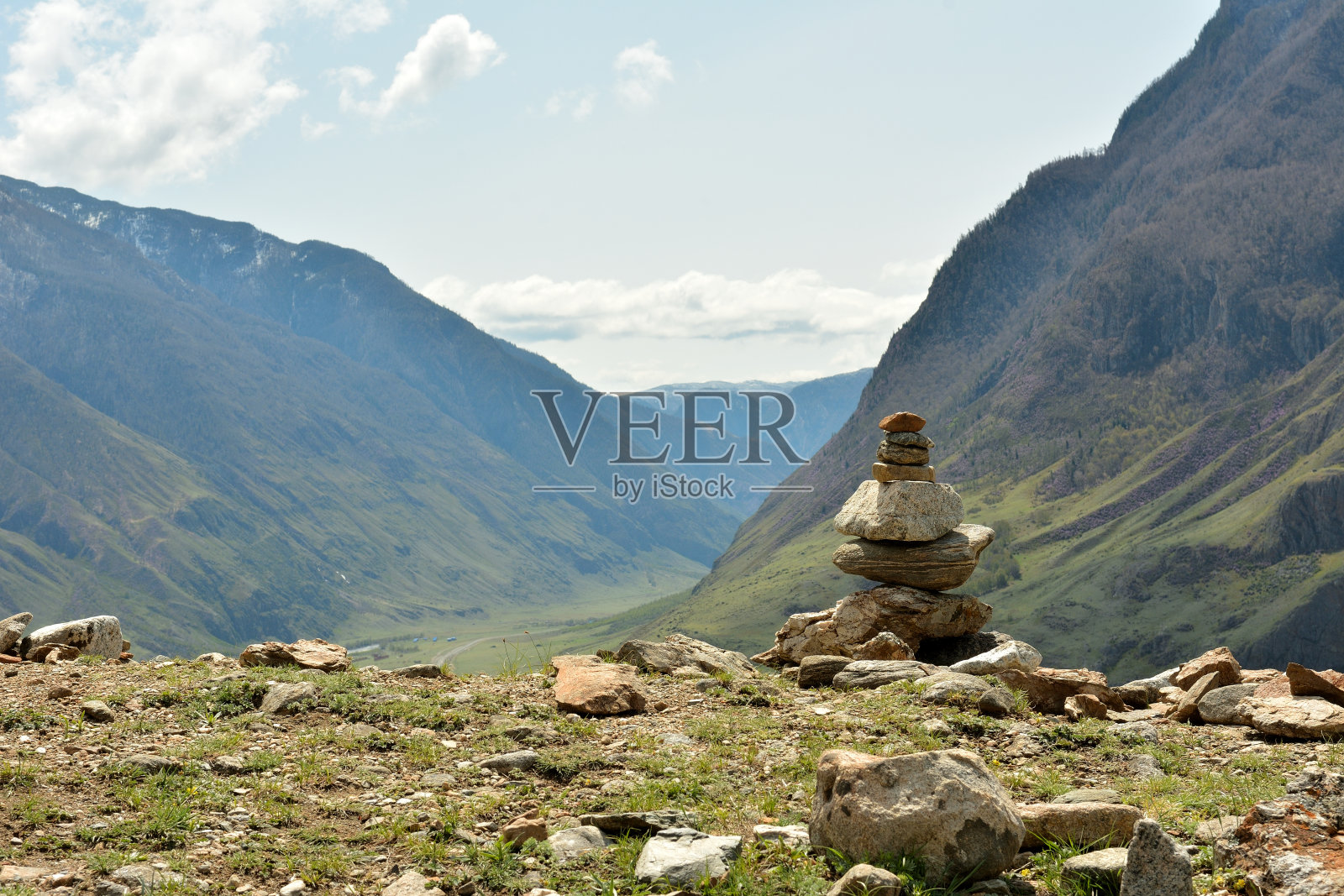 山边的一个小石头金字塔,在春天晴朗的天空下俯瞰着山间风景如画的山谷。照片摄影图片