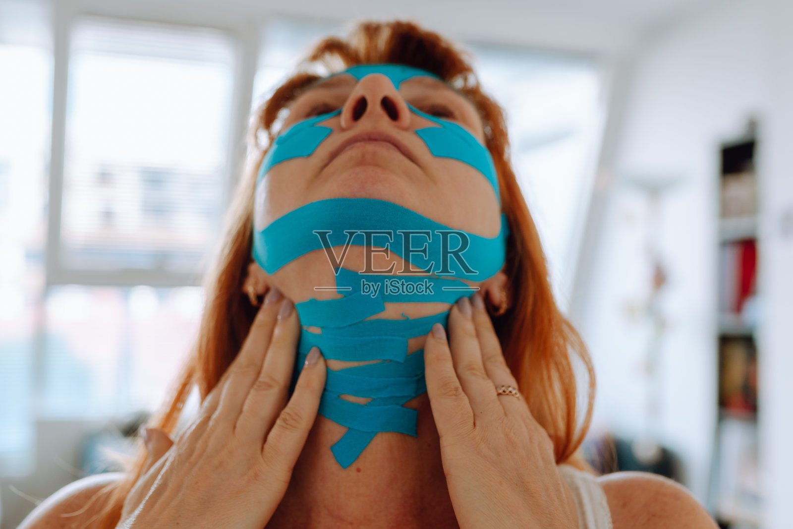 中年妇女的特写肖像,她把人体运动学胶带贴在脸上照片摄影图片