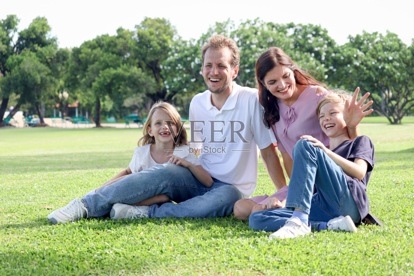 幸福的一家人坐在公园的绿草地上,微笑的父亲,母亲,儿子和女儿在周末假期一起在美丽的花园度过时光。父母和孩子在外面玩得很开心。照片摄影图片