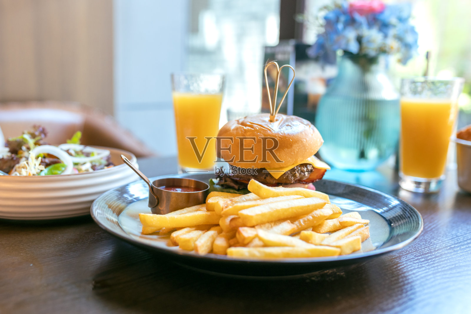 在咖啡馆或餐馆的桌子上放着汉堡、薯条和橙汁照片摄影图片