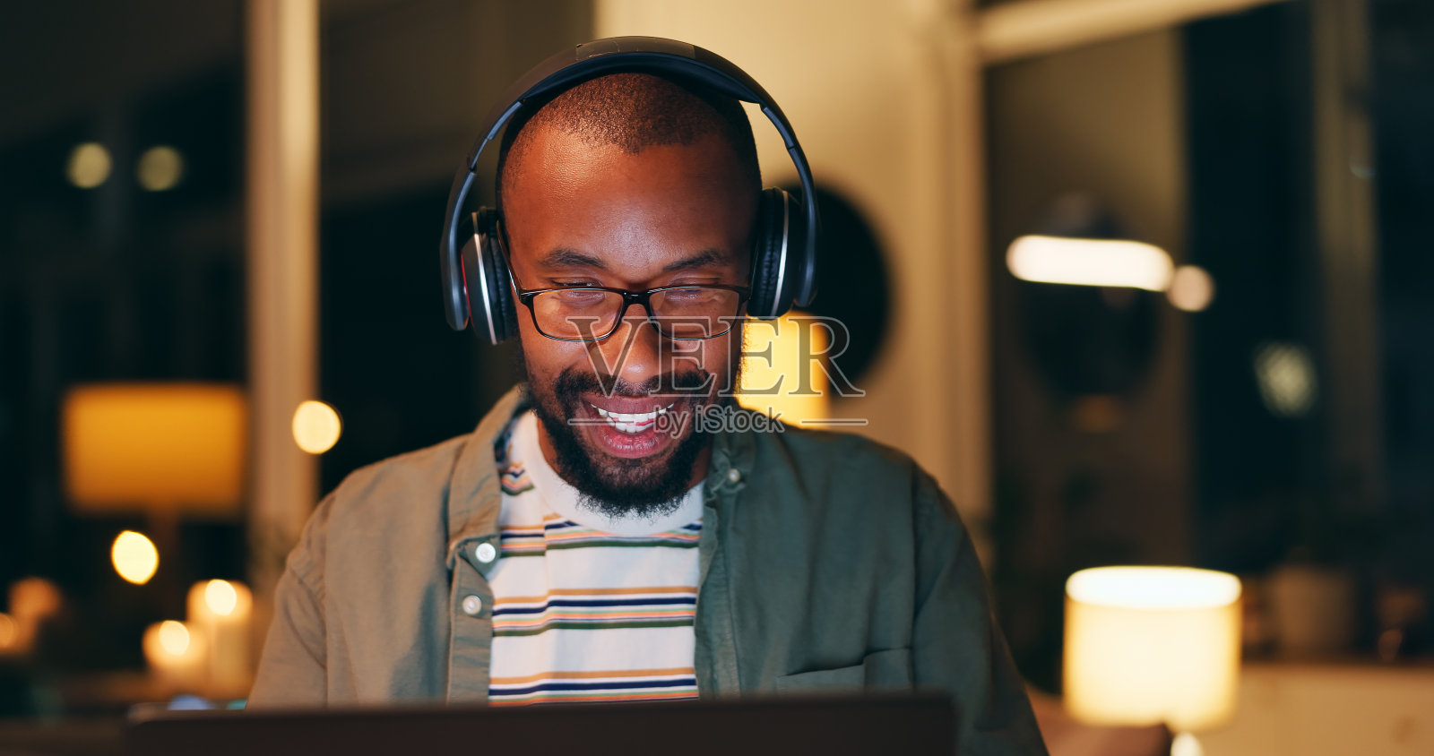 晚上,戴上耳机,办公室里的黑人拿着笔记本电脑听音乐、专辑或播放列表。微笑,有创意,在设计机构用电脑处理项目截止日期,提案或反馈照片摄影图片