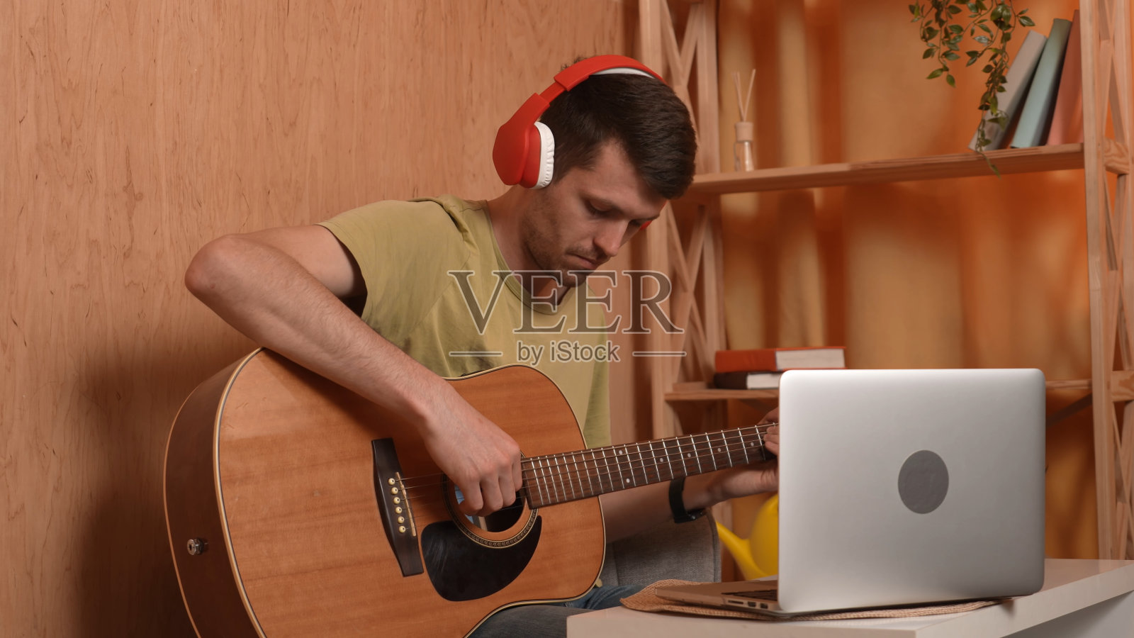 成年吉他手坐在房间里弹原声吉他,戴着耳机在笔记本电脑上观看课程,在线学习。业余爱好和休闲时间的概念。照片摄影图片