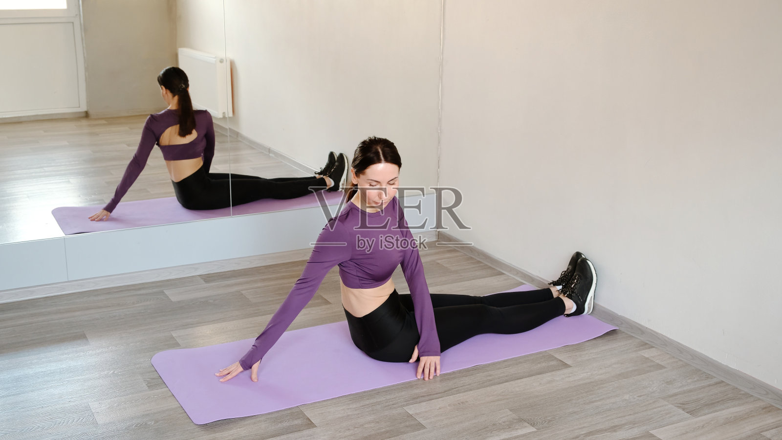 30岁的运动女性正在做伸展运动,坐在橡胶垫子上,身体向两侧旋转。运动女孩将她的躯干从一边转到另一边。变暖的肌肉。健康生活理念。4 k照片摄影图片