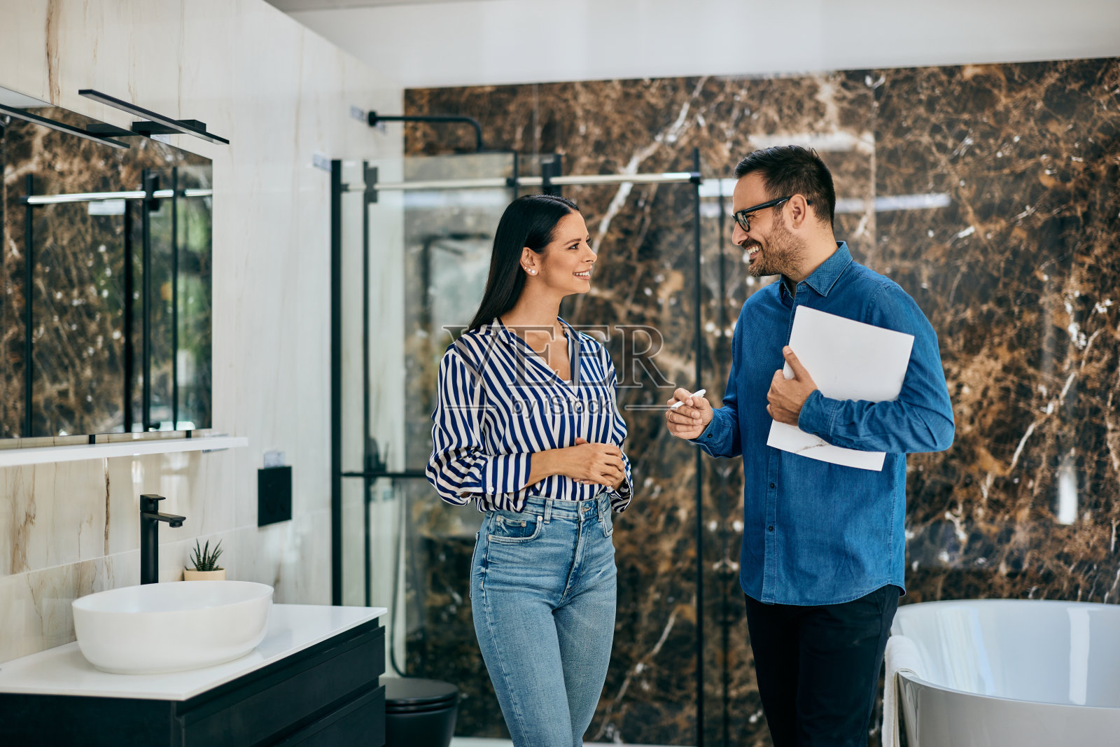 在家具店,男卖家站在家具浴室里和女顾客聊天。照片摄影图片