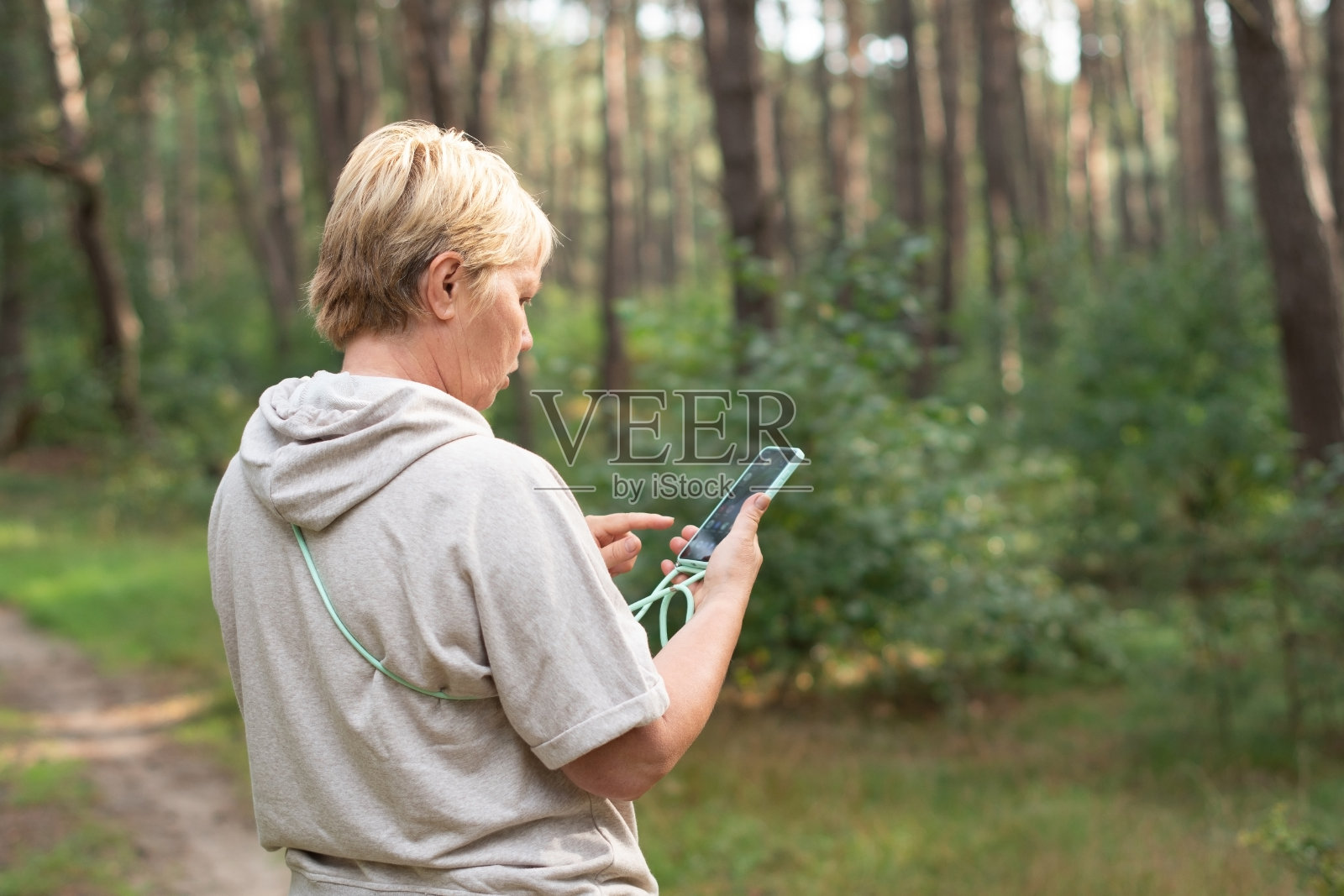 森林里穿着米色针织西装的女人每天都要走几步,她在松林里呼吸着空气,看了看智能手机上的路线图,启动了计步器,照片摄影图片