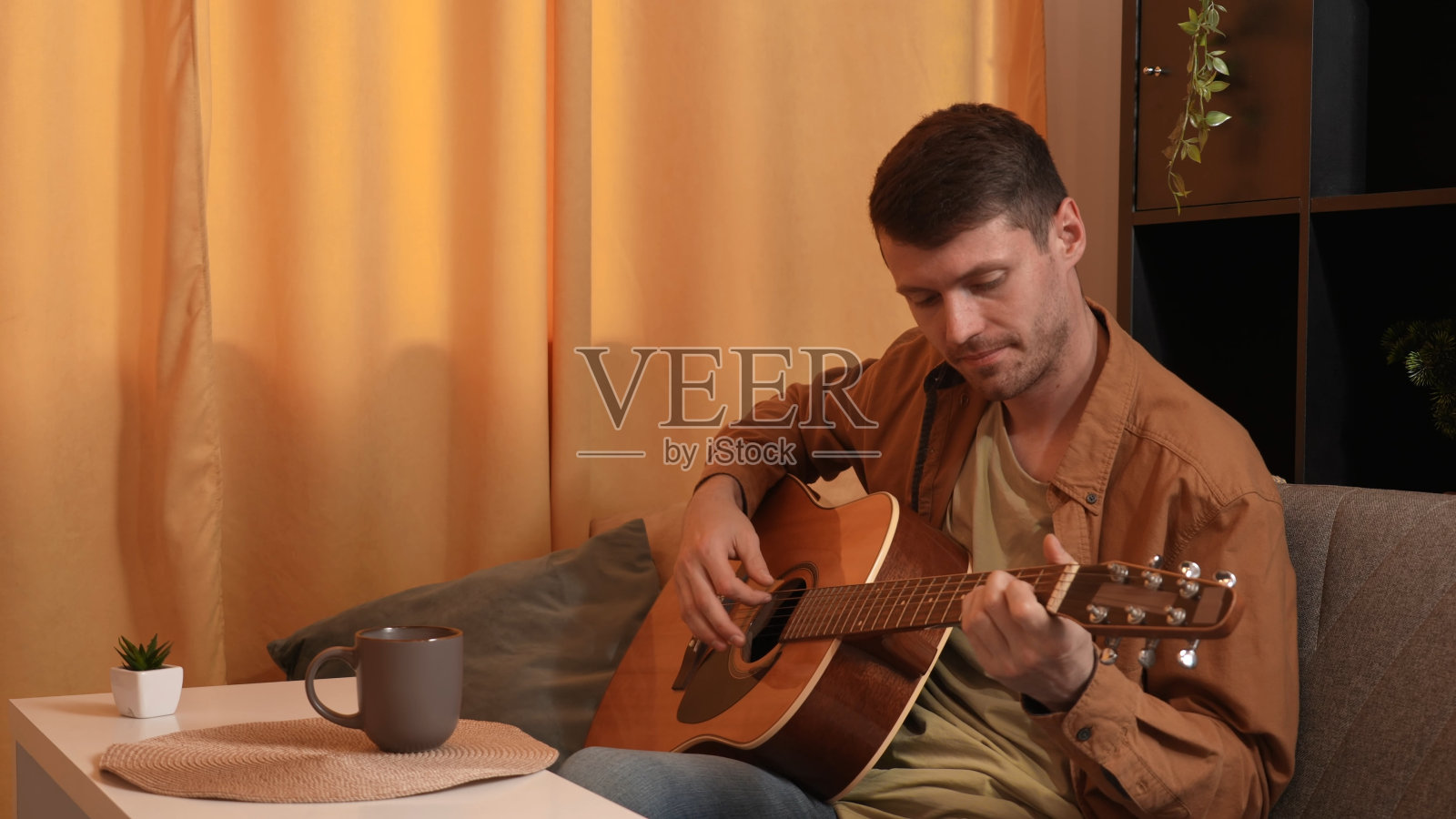 成年吉他手坐在房间里弹原声吉他,谱曲,指法和弦。业余爱好和休闲时间的概念。照片摄影图片