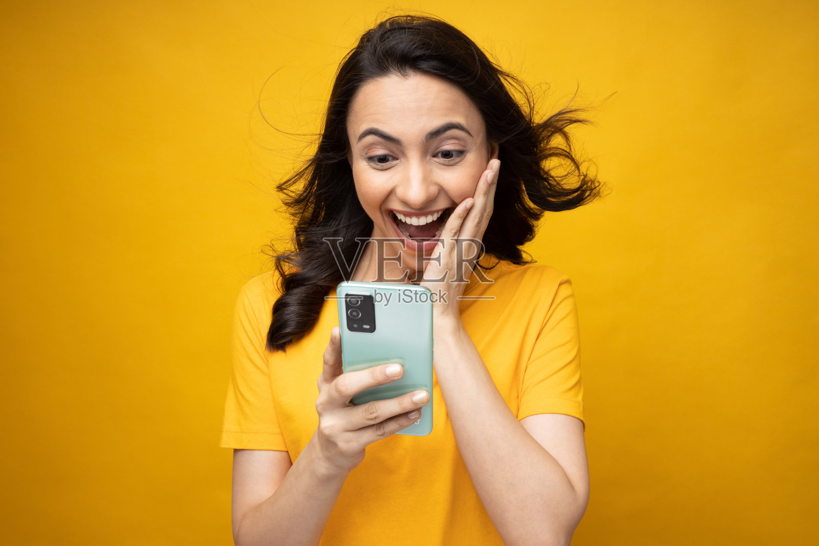 年轻女子正在展示用手机隔离的黄色背景照片照片摄影图片