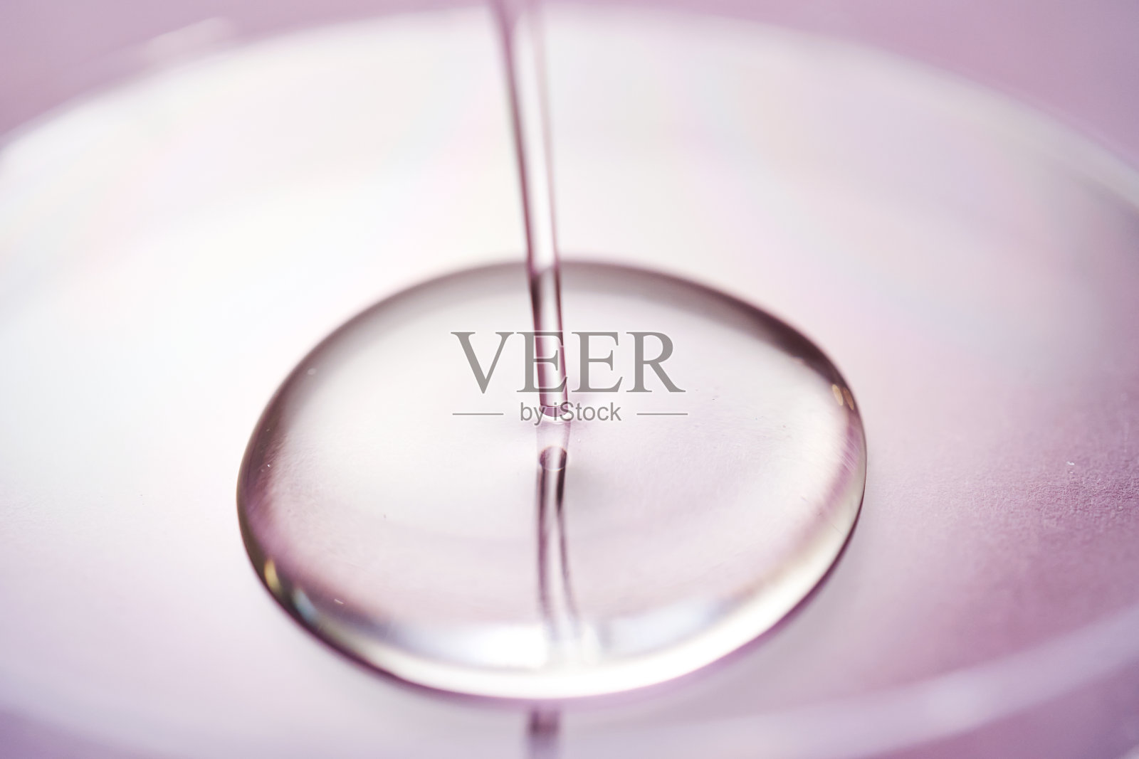 精华液或化妆品油流入紫色背景的透明碗中。照片摄影图片