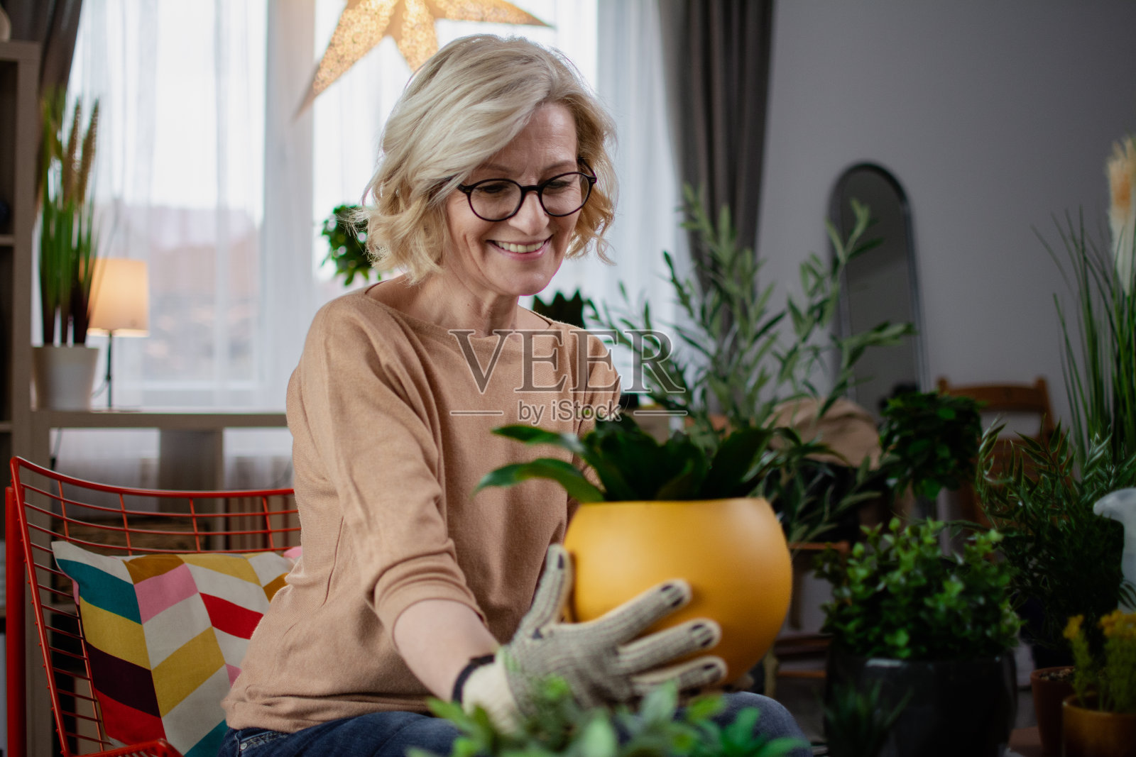 一个成熟的金发卷发女人坐在椅子上,在花盆里插花照片摄影图片