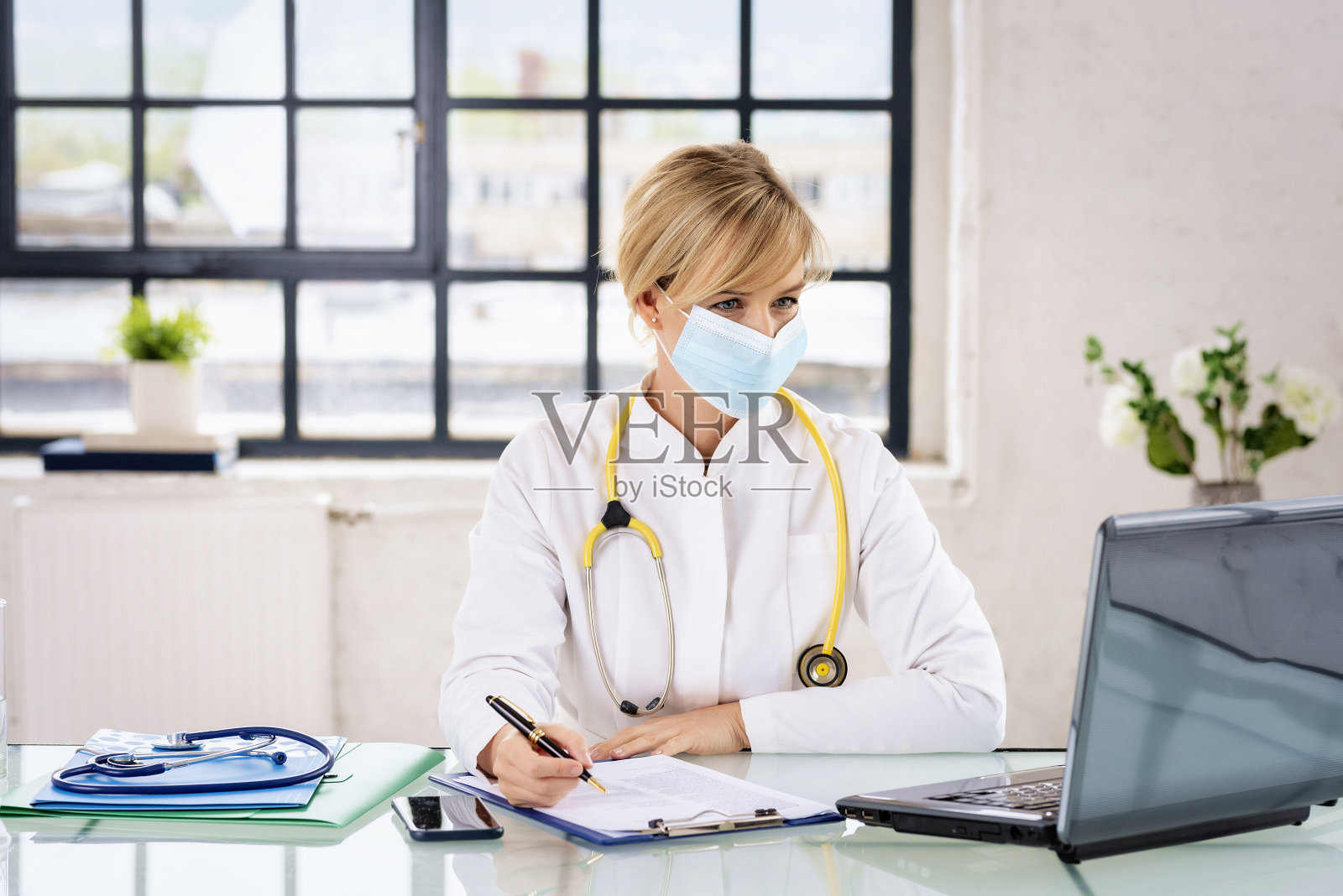 戴着外科口罩的女医生坐在医生的房间里,使用笔记本电脑工作照片摄影图片