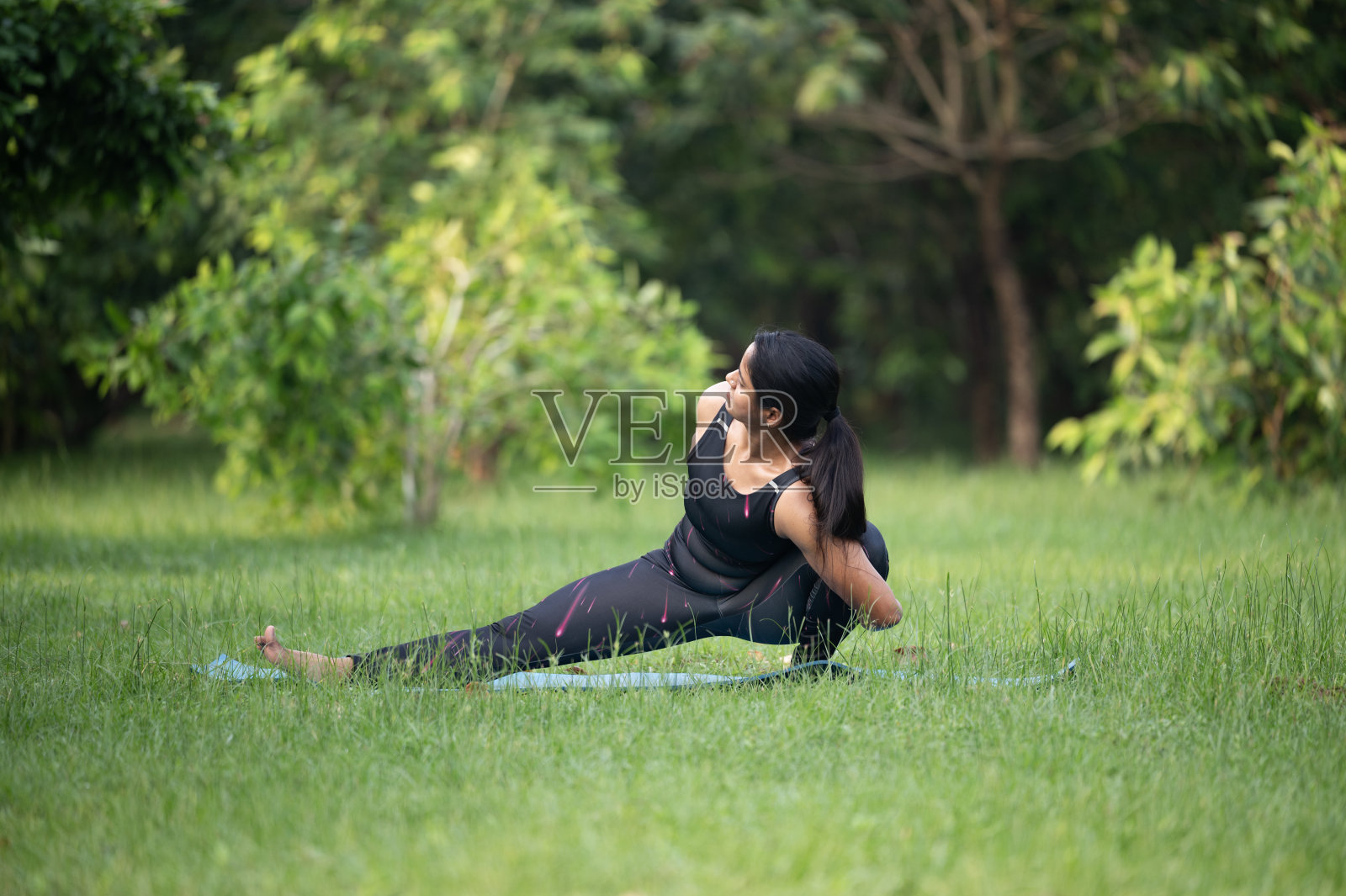 年轻女子在绿色公园户外练习瑜伽照片摄影图片