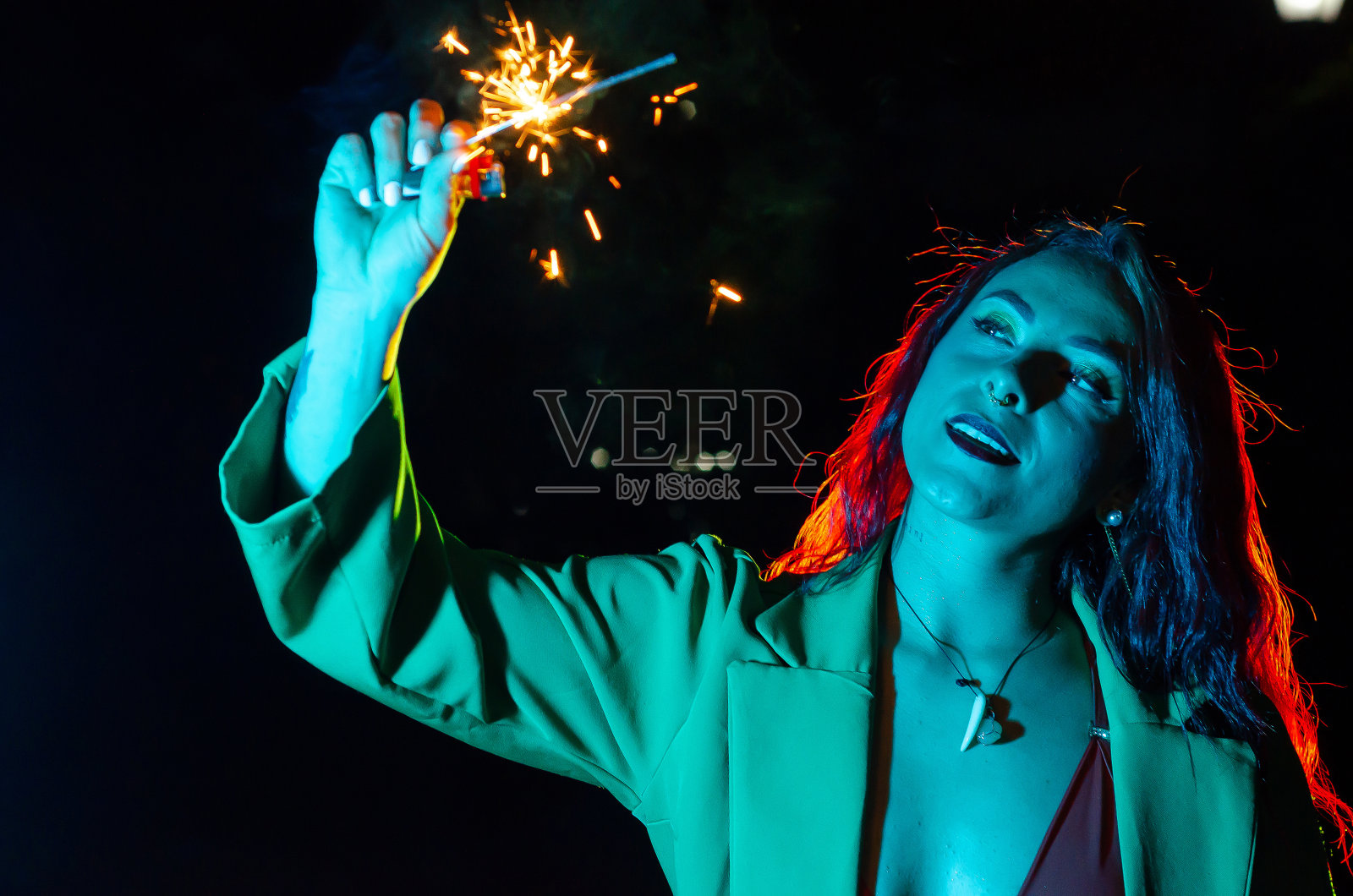 美丽的年轻红发女子的肖像,在彩色led灯的照亮下,在晚上玩着烟花照片摄影图片