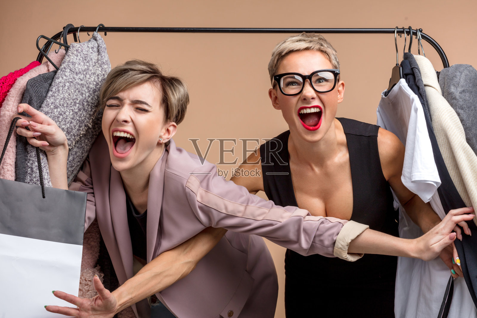 两个迷人的女孩正在争夺最后一件时髦的连衣裙照片摄影图片