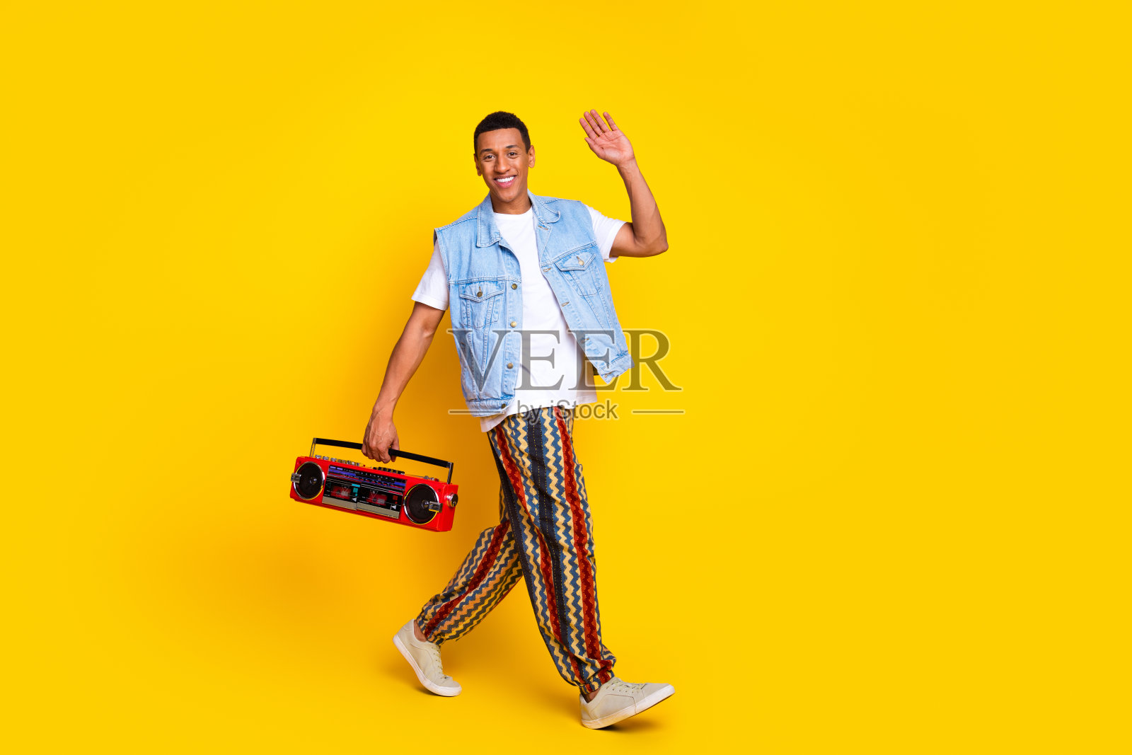 快乐的家伙穿着牛仔裤马甲的全身照片拿着音箱说嗨走空空间孤立的黄色背景照片摄影图片