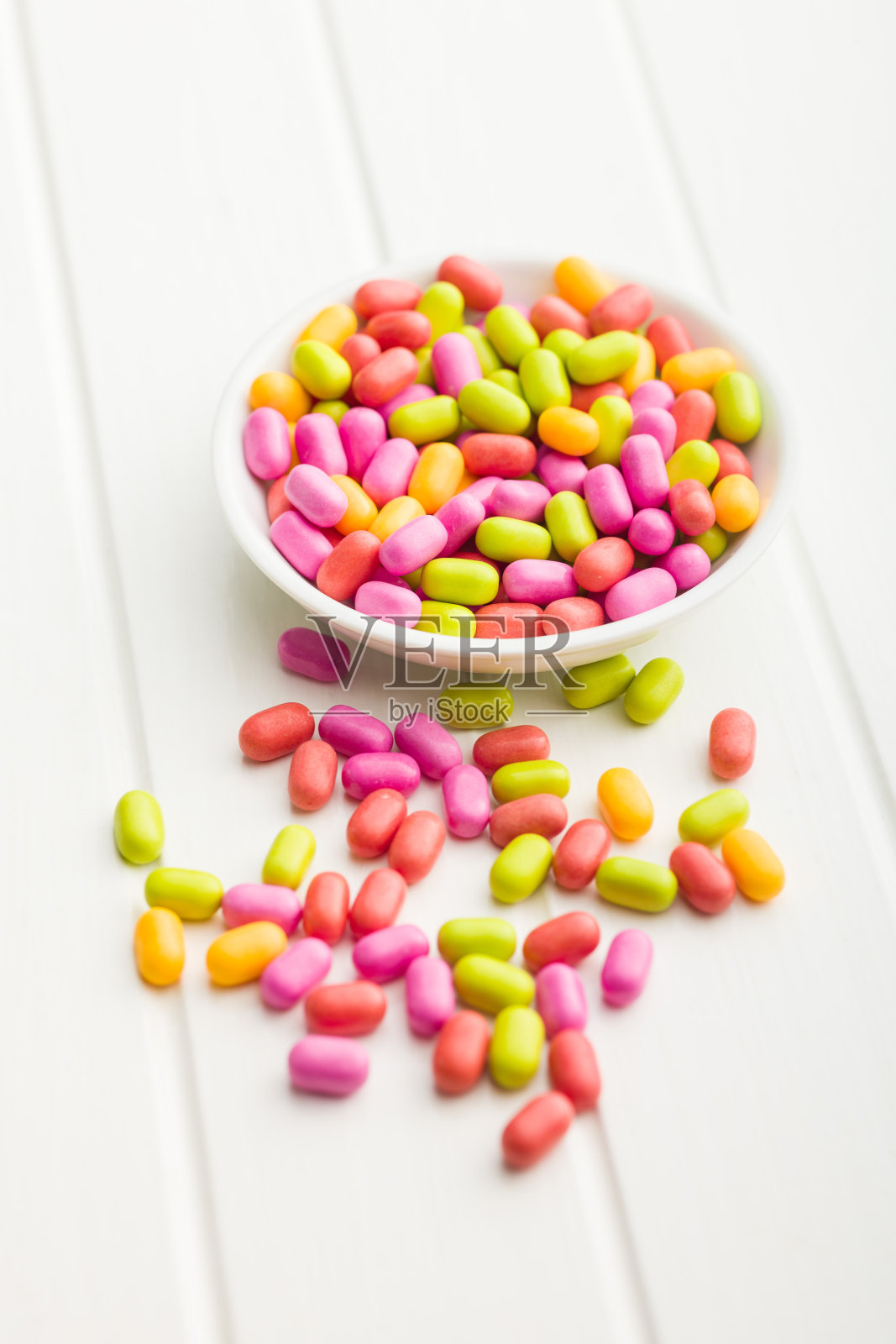 白色桌子上的碗里装着五颜六色的硬薄荷糖。照片摄影图片