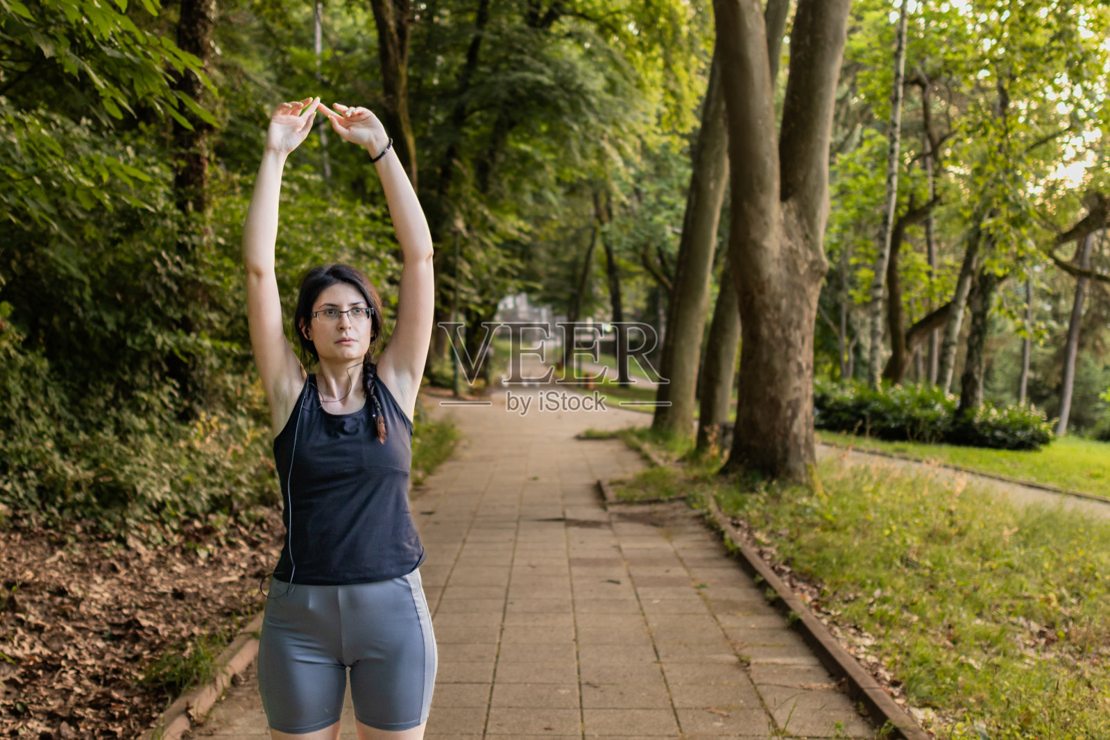 穿着健身服的年轻漂亮的女人在公园里做体育锻炼。她在跑步前做伸展运动。照片摄影图片